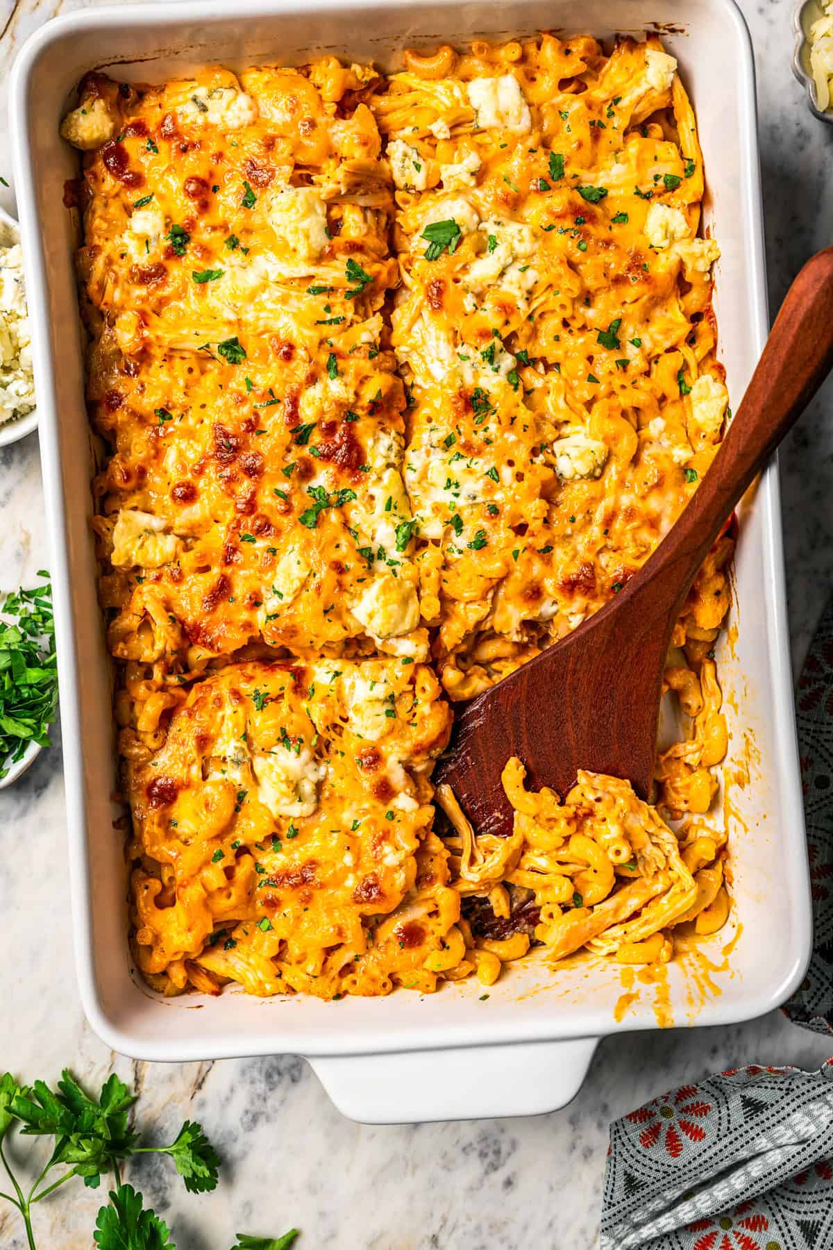 Overhead view of a wooden serving spoon resting in an open serving of buffalo mac and cheese in a casserole dish.