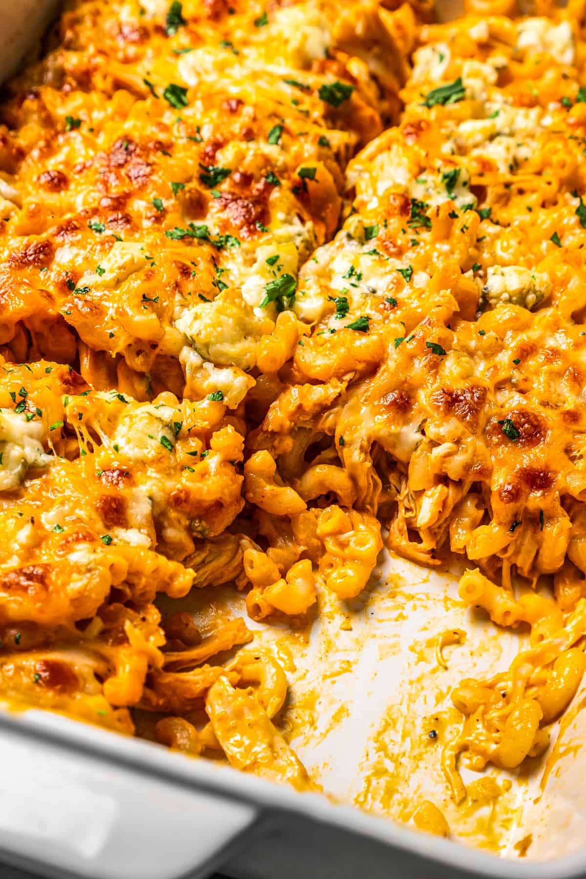 Close up of buffalo mac and cheese in a casserole dish with a serving missing.