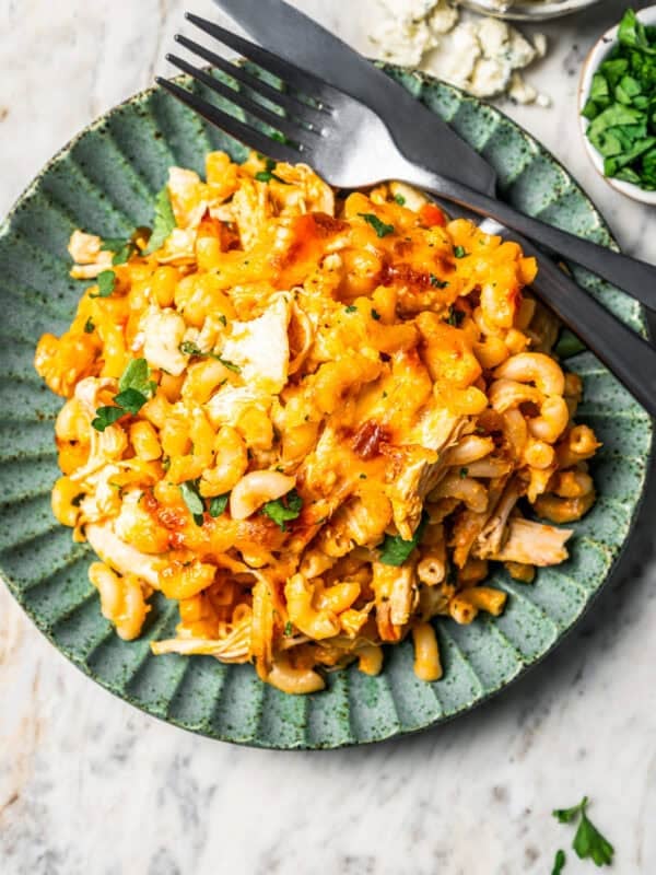 Serving of buffalo mac and cheese on a green stoneware plate next to a fork and knife.