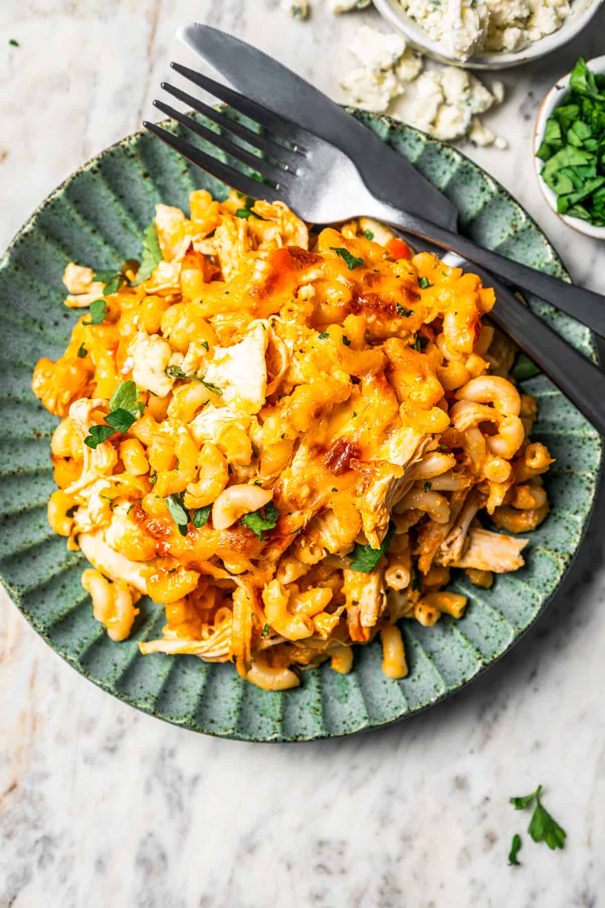 Serving of buffalo mac and cheese on a green stoneware plate next to a fork and knife.