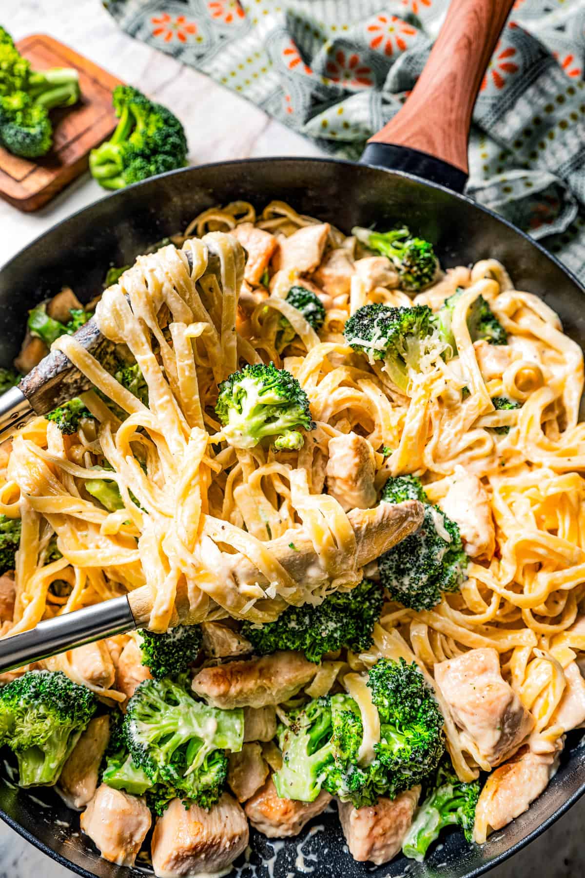 Pair of tongs resting in a pan of chicken fettuccine.