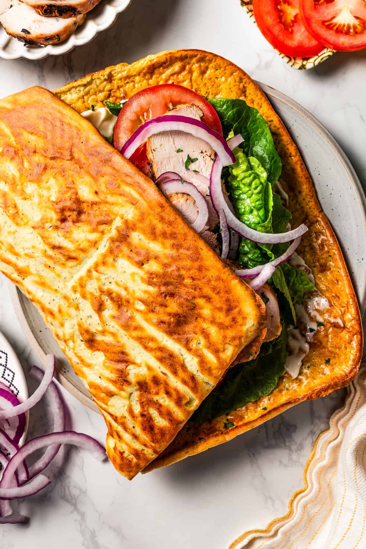 Overhead view of a cottage cheese flatbread partially folded in half over lettuce, tomatoes, onions, and chicken slices.