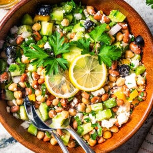 A bean salad garnished with lemon slices in a wooden bowl with a pair of salad tongs.