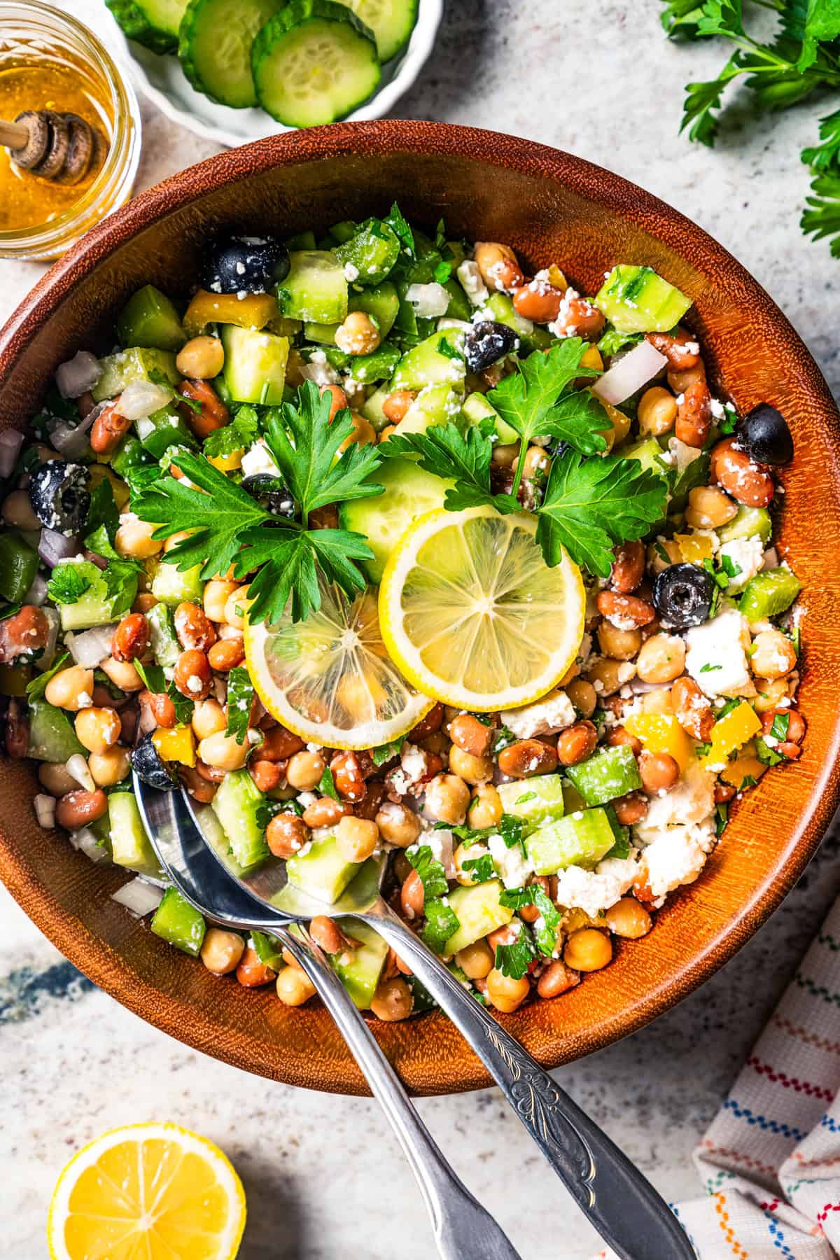 A bean salad garnished with lemon slices in a wooden bowl with a pair of salad tongs.