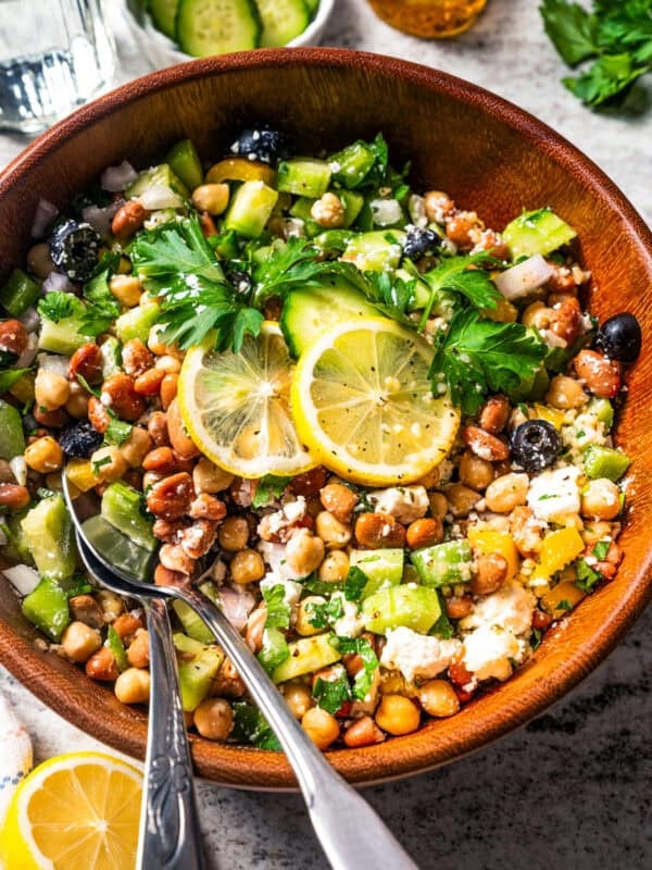 Dense bean salad in a wooden bowl with a pair of salad tongs.