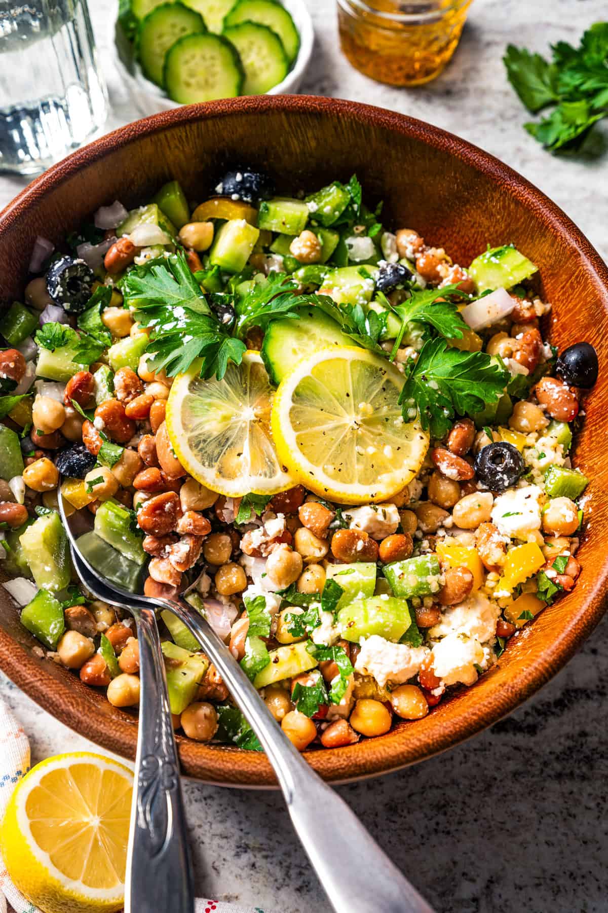 Dense bean salad in a wooden bowl with a pair of salad tongs.