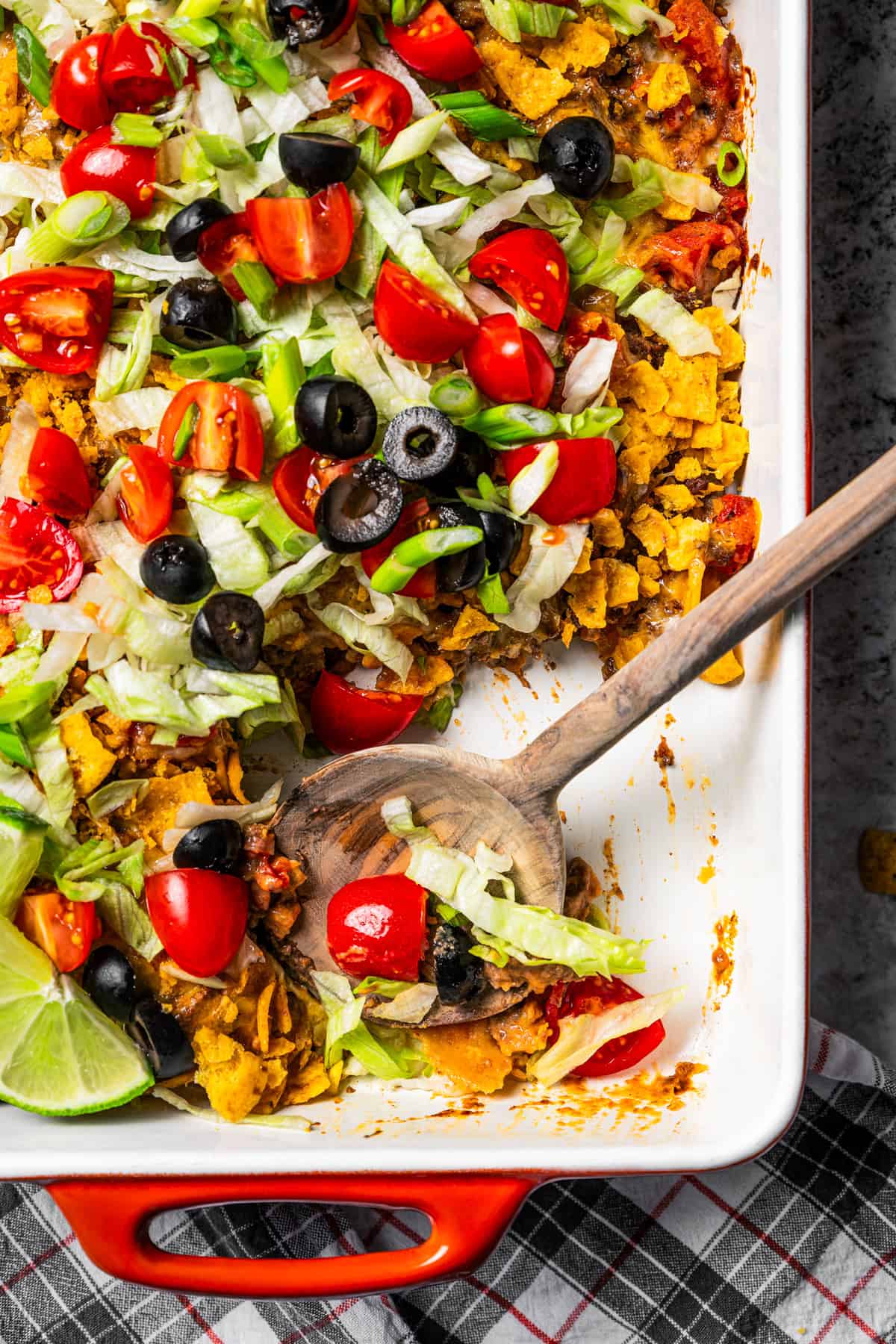 Overhead view of a walking taco casserole with a serving spoon resting in an open corner of the baking dish.