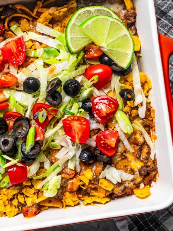 Close-up shot of a taco casserole in a baking dish garnished with olives, tomatoes, and shredded lettuce.