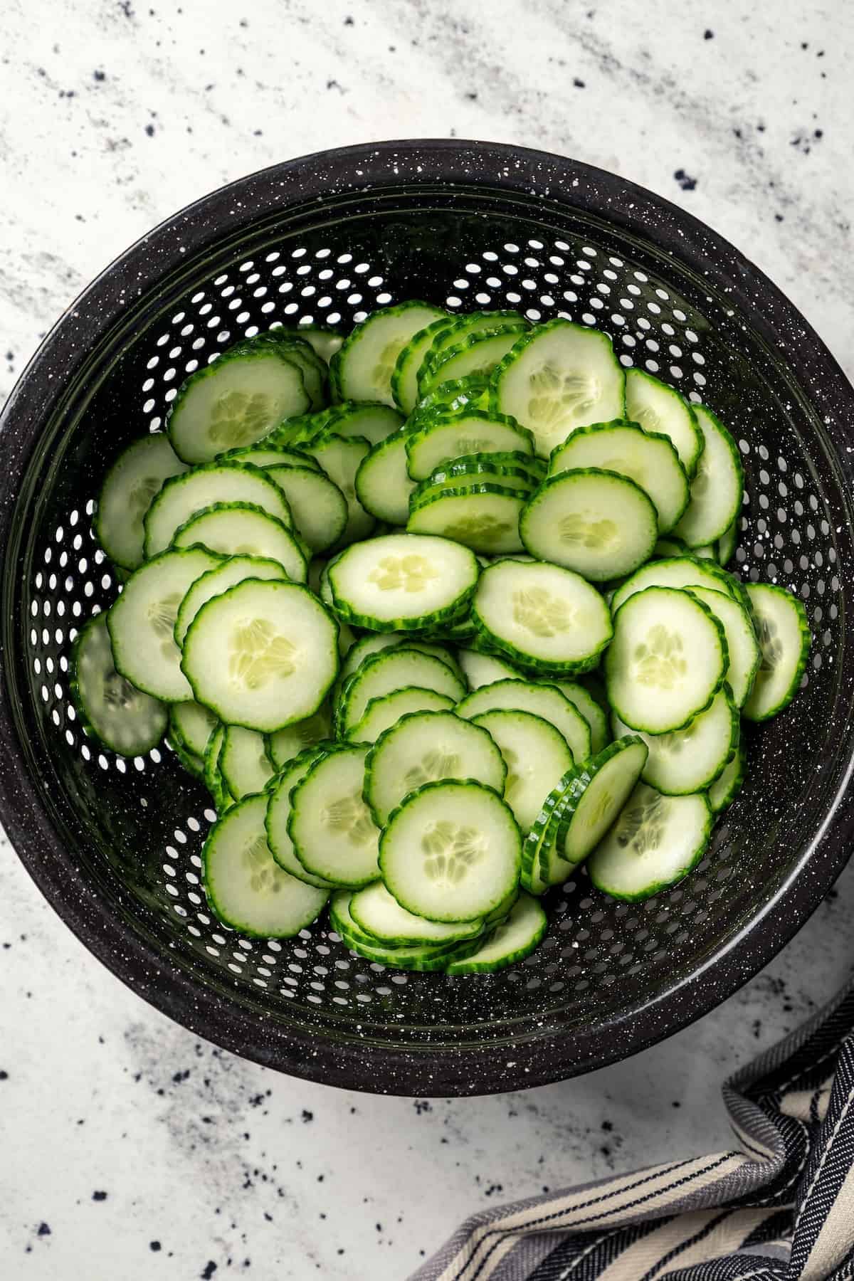 Sliced and drained cucumbers in a black colander.