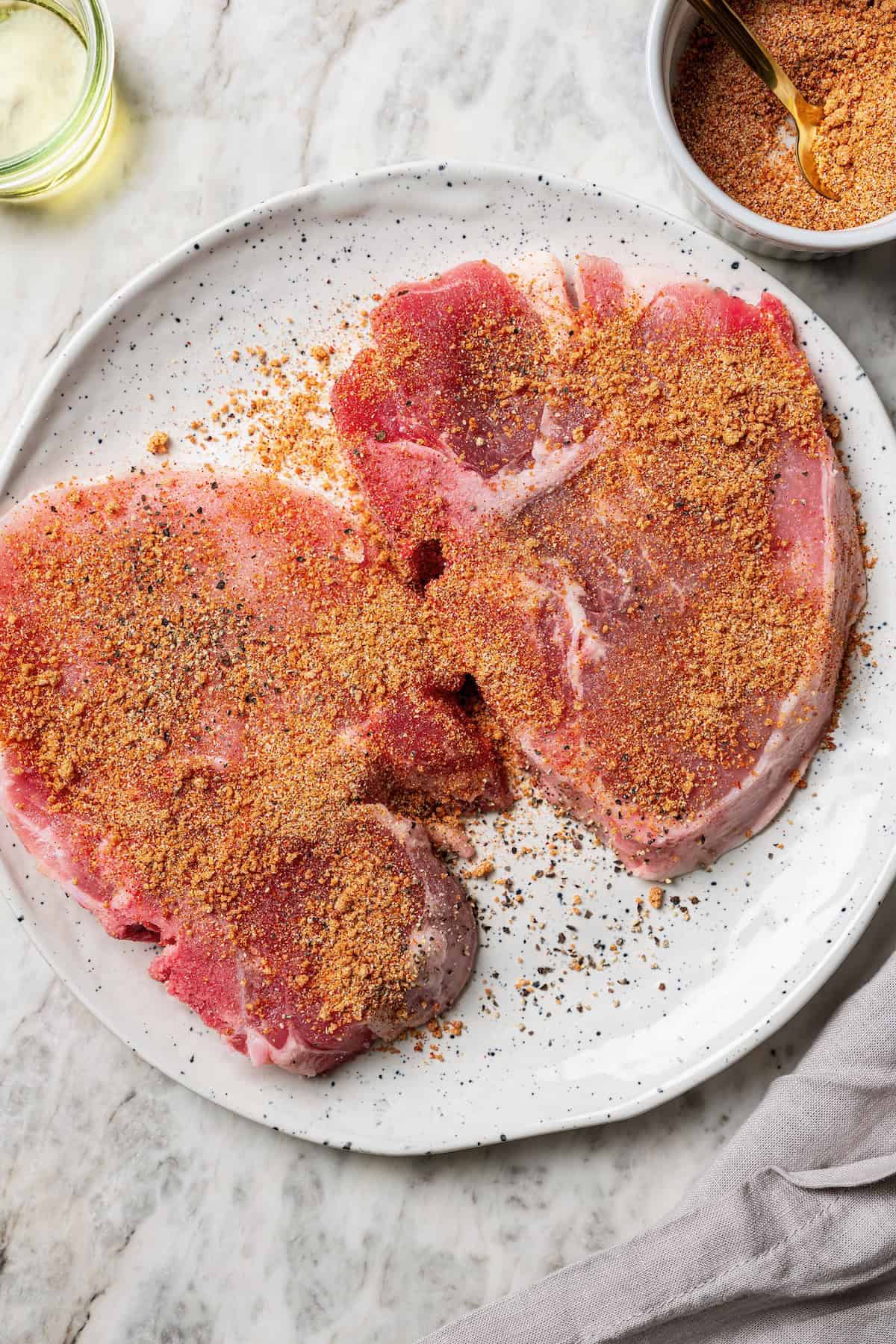 Two seasoned pork steaks on a white plate.