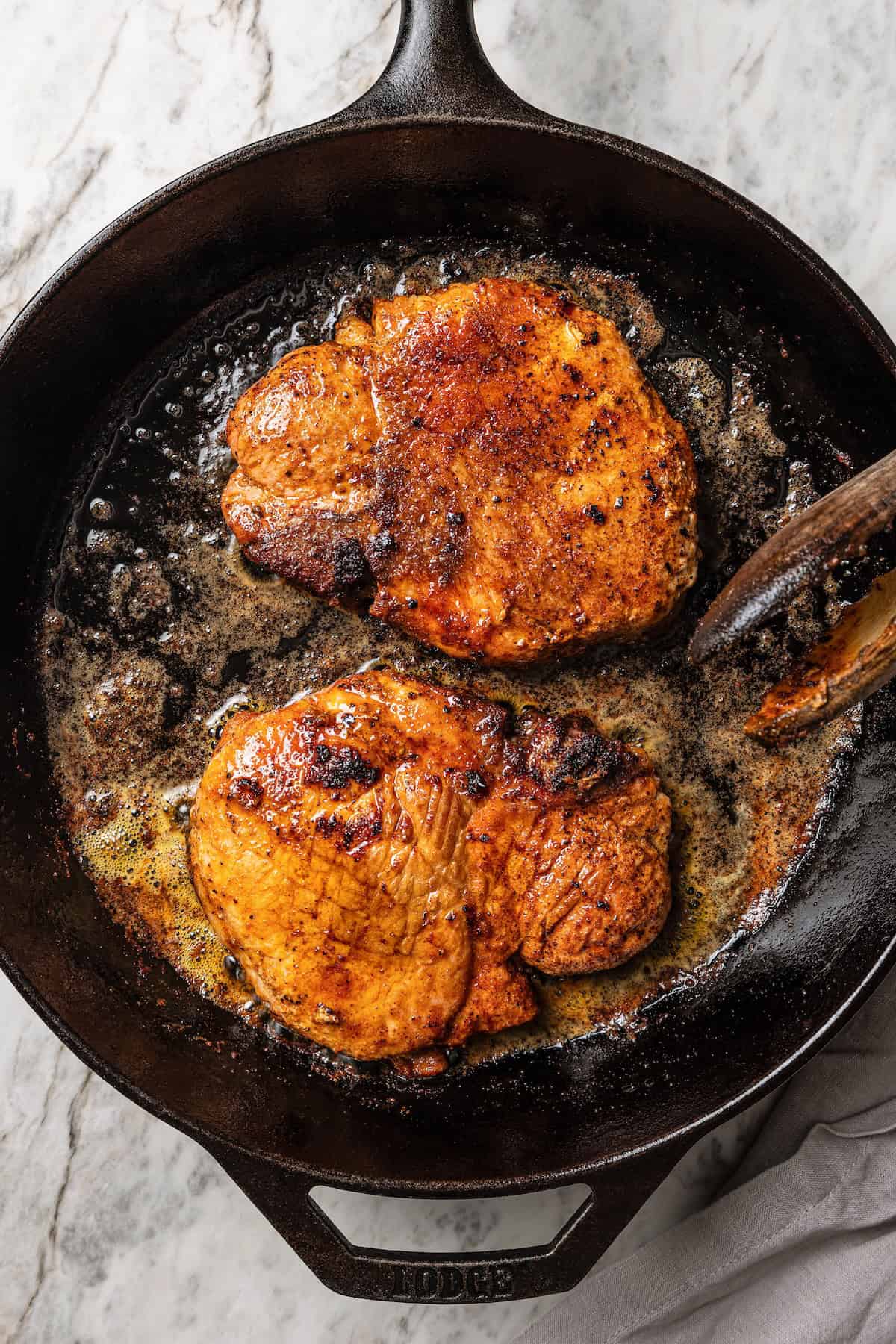 Two pork steaks searing in a cast iron skillet.