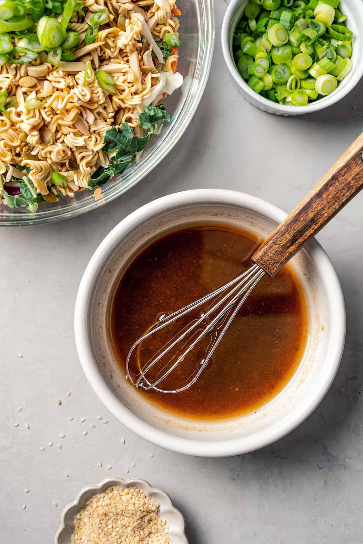 Salad dressing whisked together in a white bowl next to a larger bowl of salad.