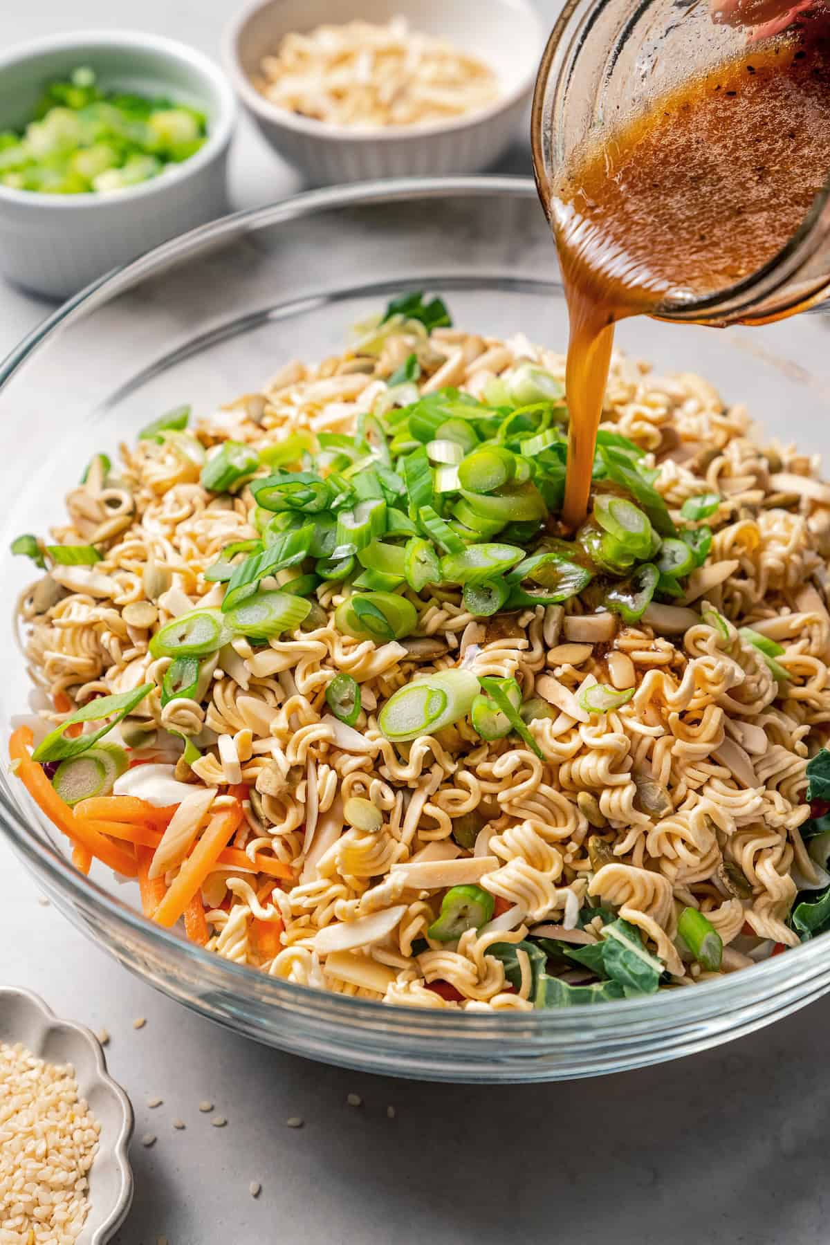 Dressing being poured over ramen salad ingredients in a large glass bowl.