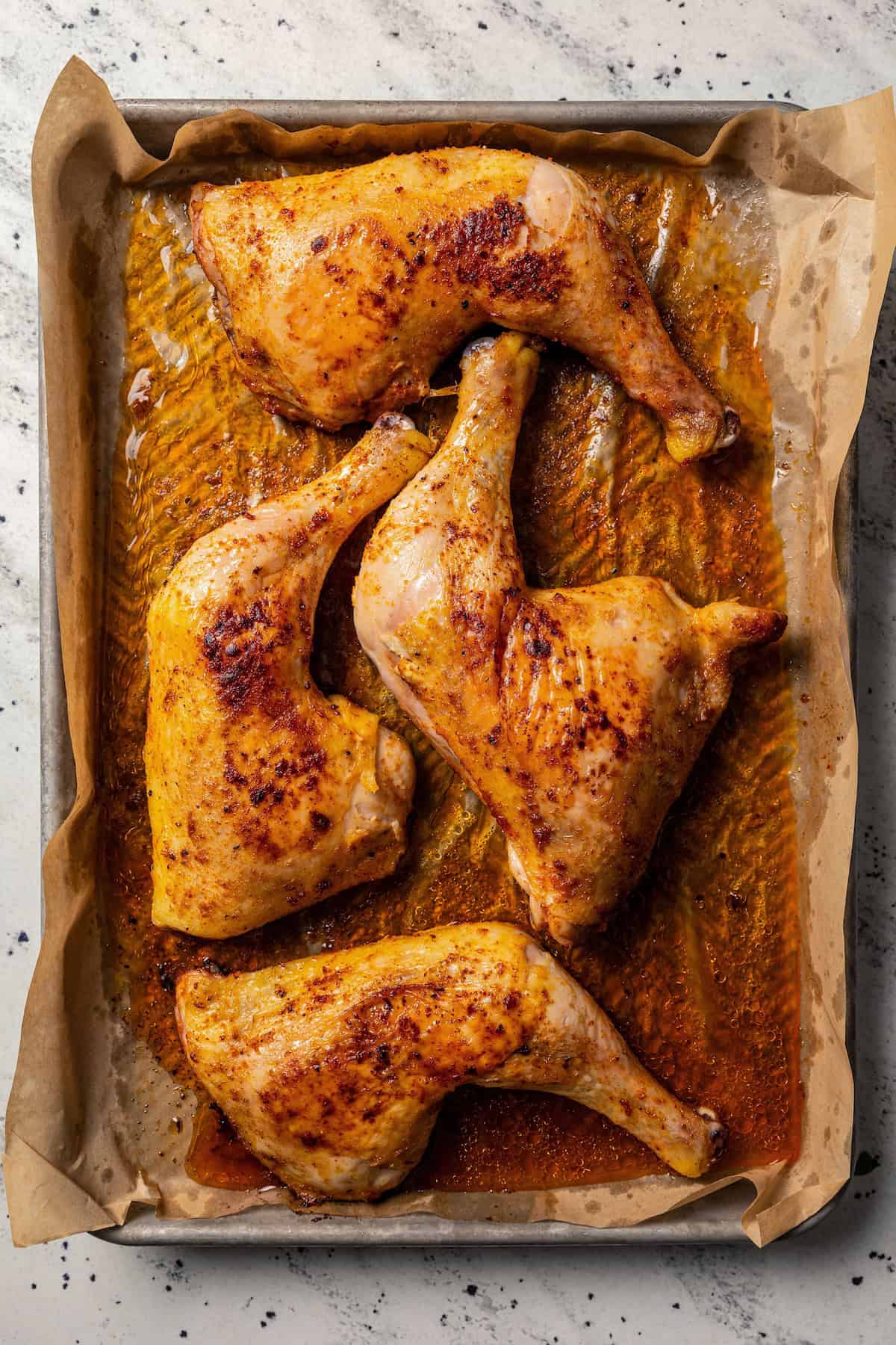 Overhead view of roasted chicken leg quarters on a baking pan.