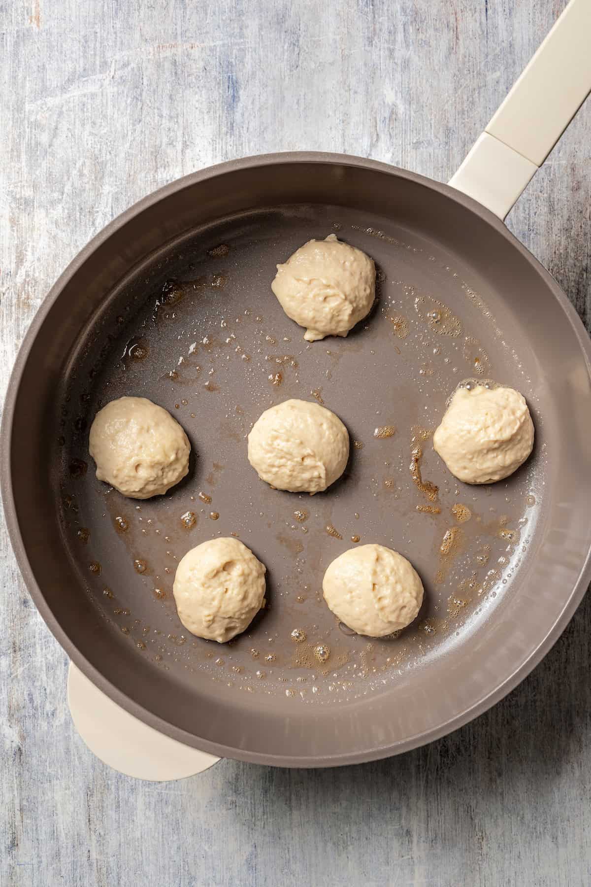 Dollar-sized pancake batter portions in a skillet.