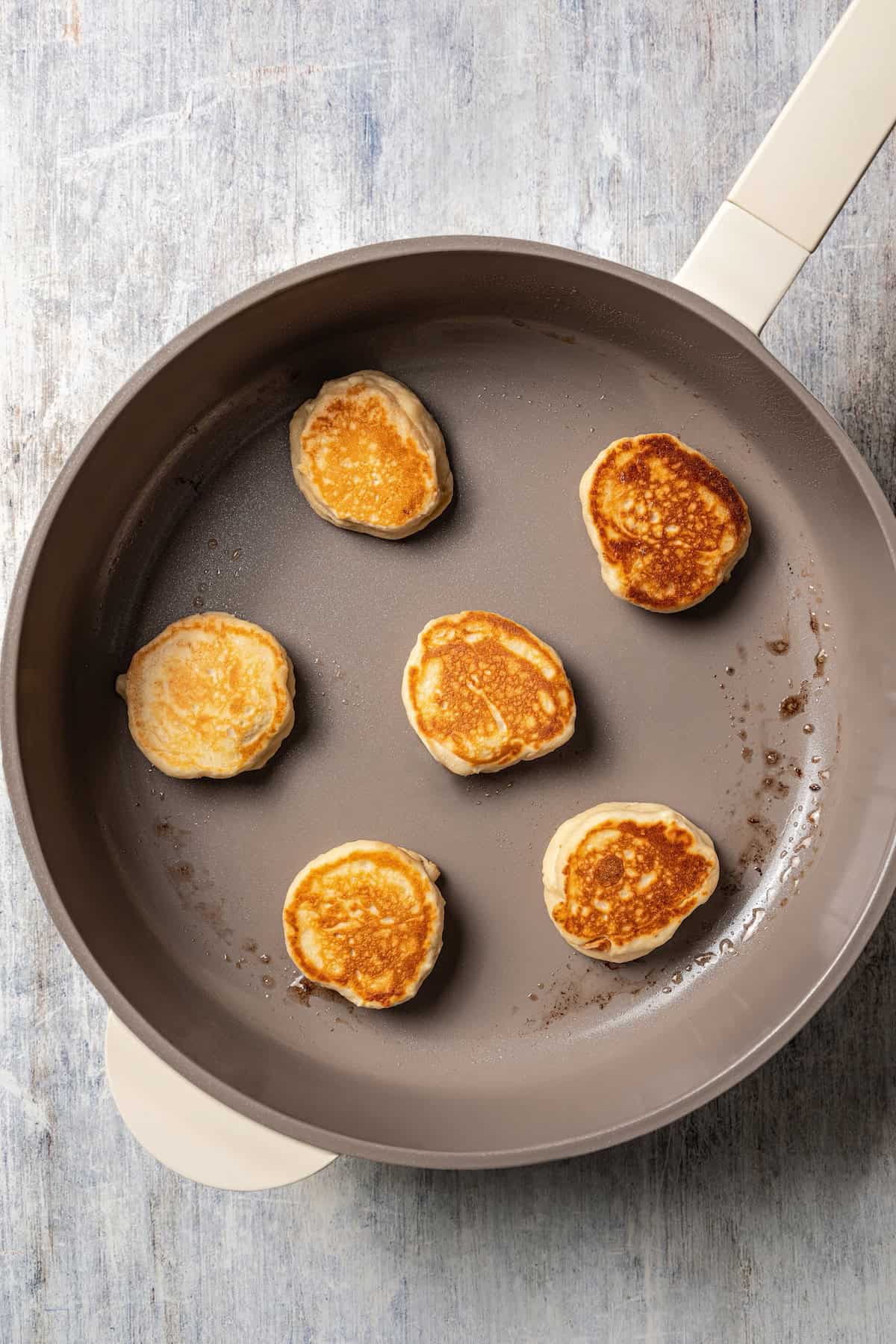 Silver dollar pancakes cooking in a skillet.