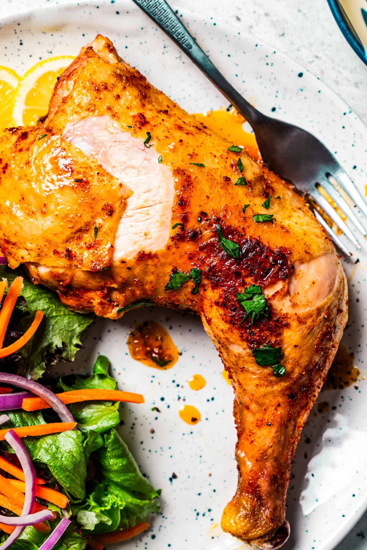 Chicken leg quarter served on a plate with a side of salad.