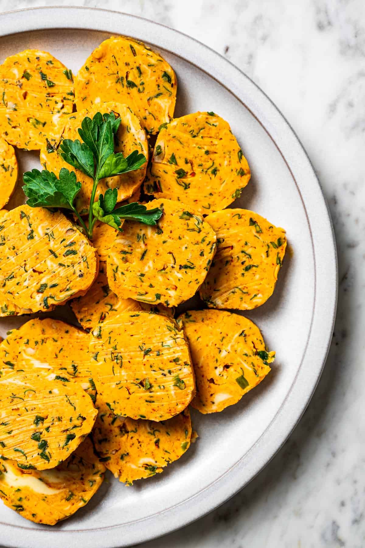 Round slices of cowboy butter stacked on a white plate, garnished with parsley.