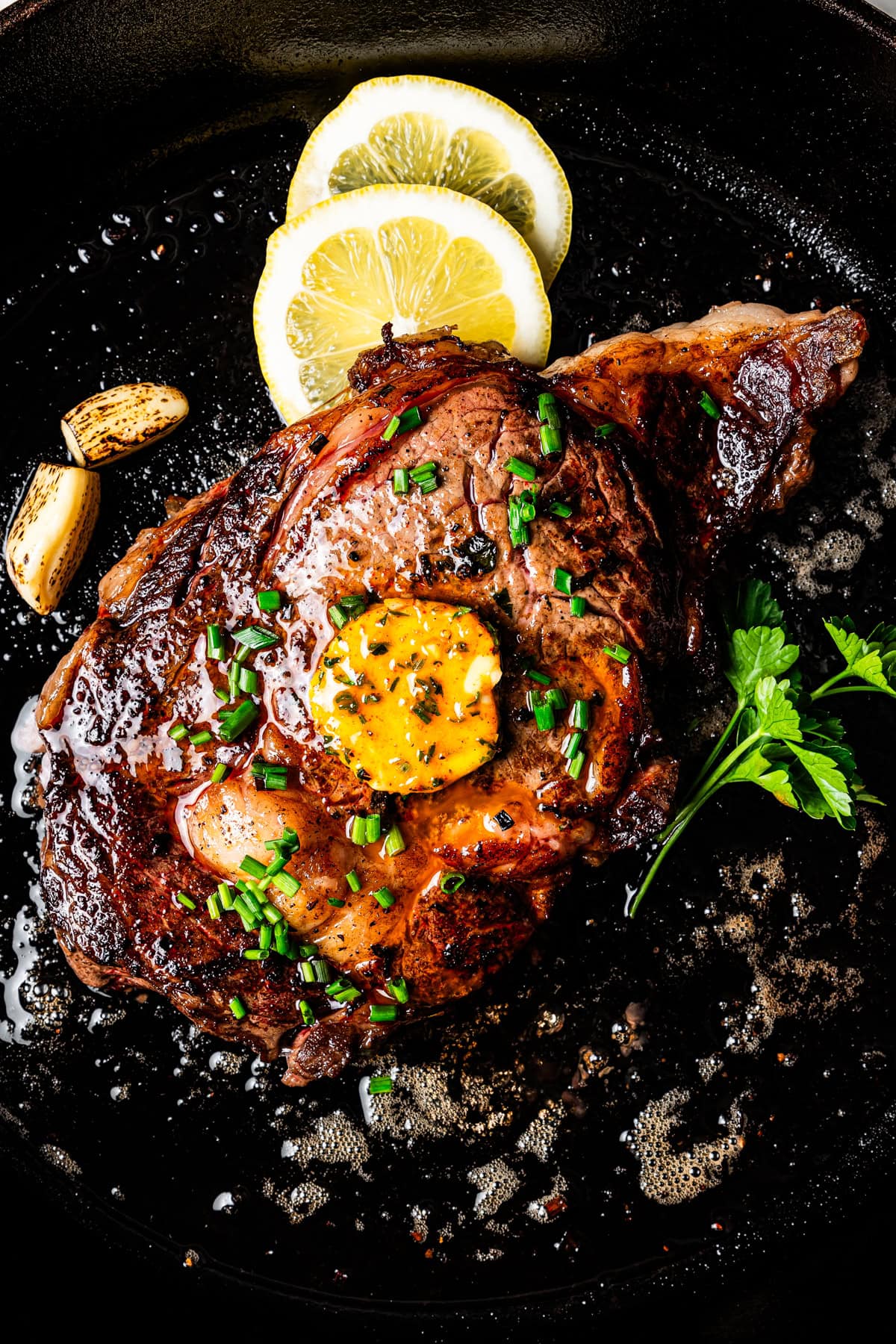 A steak topped with a pat of cowboy butter in a skillet.