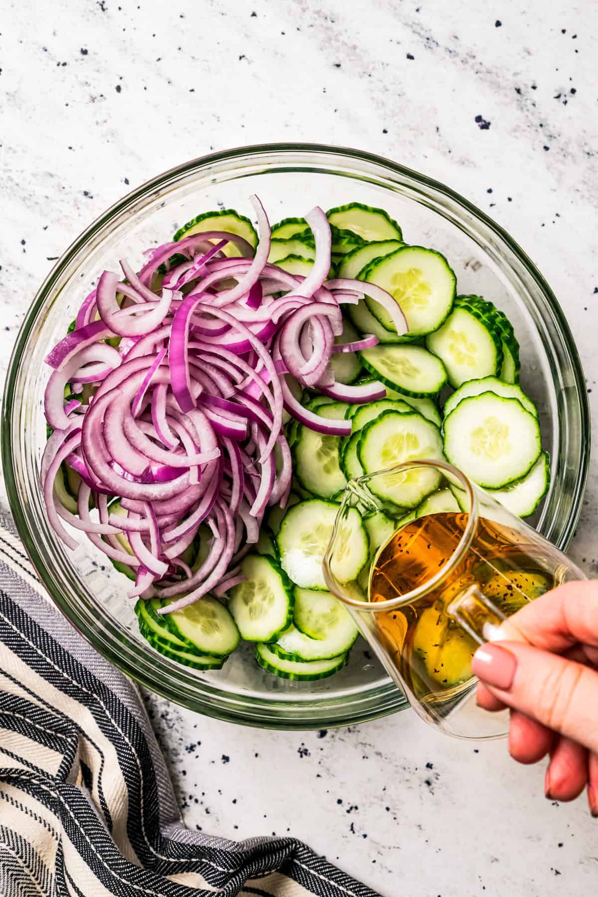 Pouring dressing over sliced red onions and sliced cucumbers.