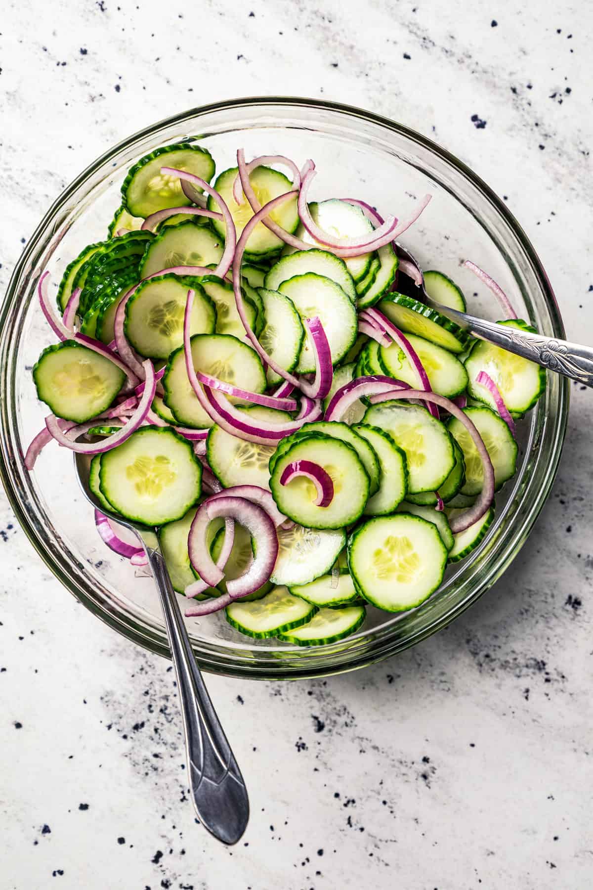 Tossing cucumber and onion salad in a glass mixing bowl.