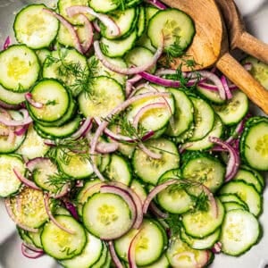 Cucumber and onion salad in a large salad bowl with two wooden salad tongs.