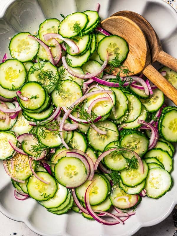 Cucumber and onion salad in a large salad bowl with two wooden salad tongs.