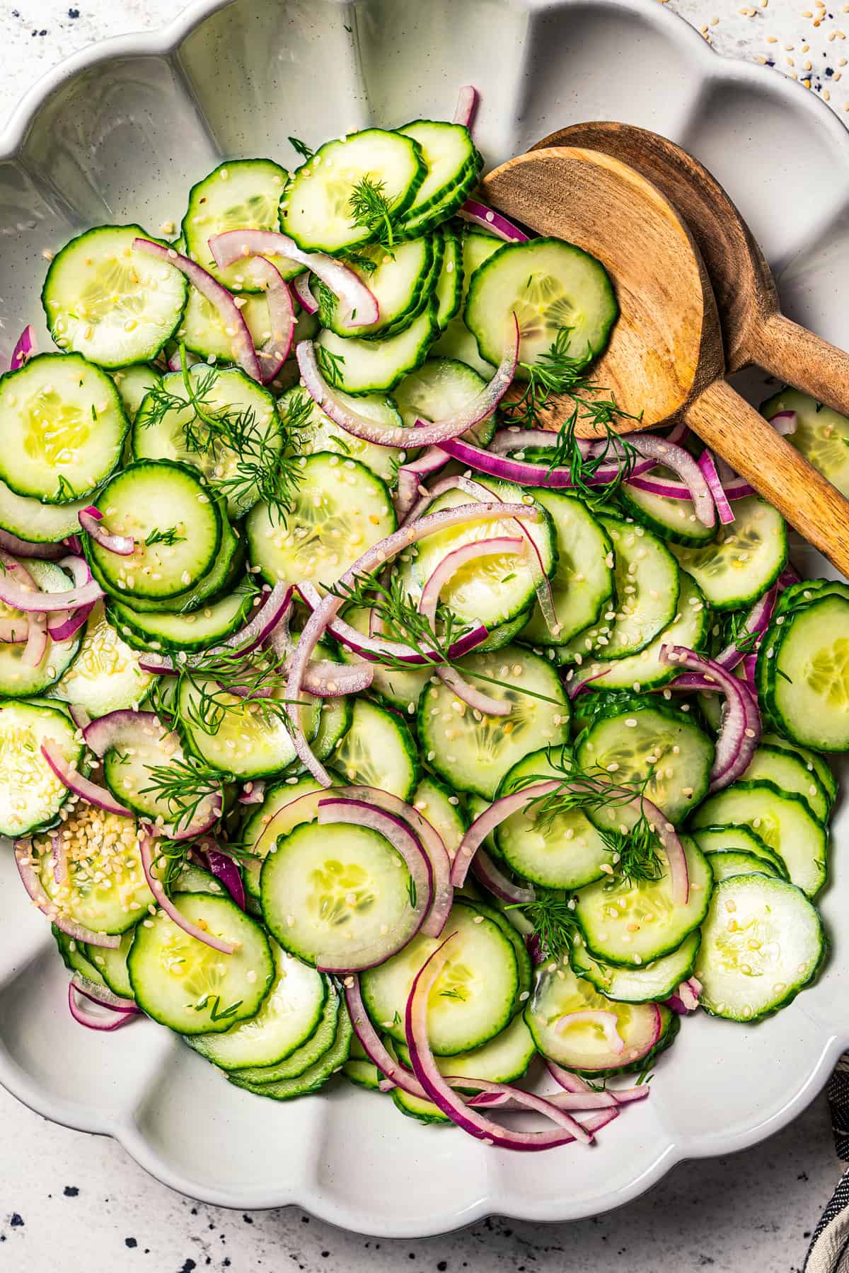 Cucumber and onion salad in a large salad bowl with two wooden salad tongs.