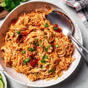 Overhead view of pulled chicken in a large bowl with two serving spoons.