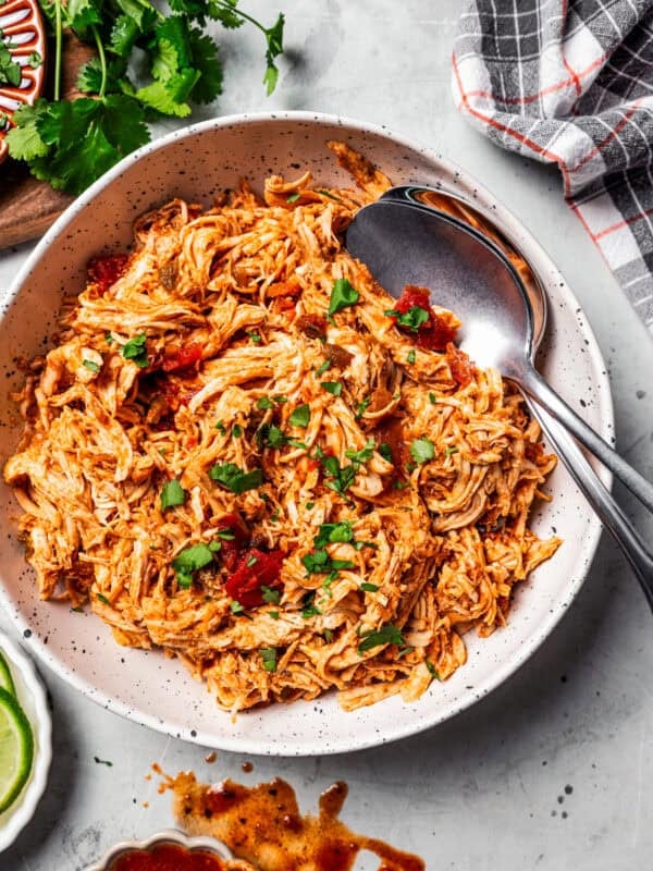 Overhead view of pulled chicken in a large bowl with two serving spoons.