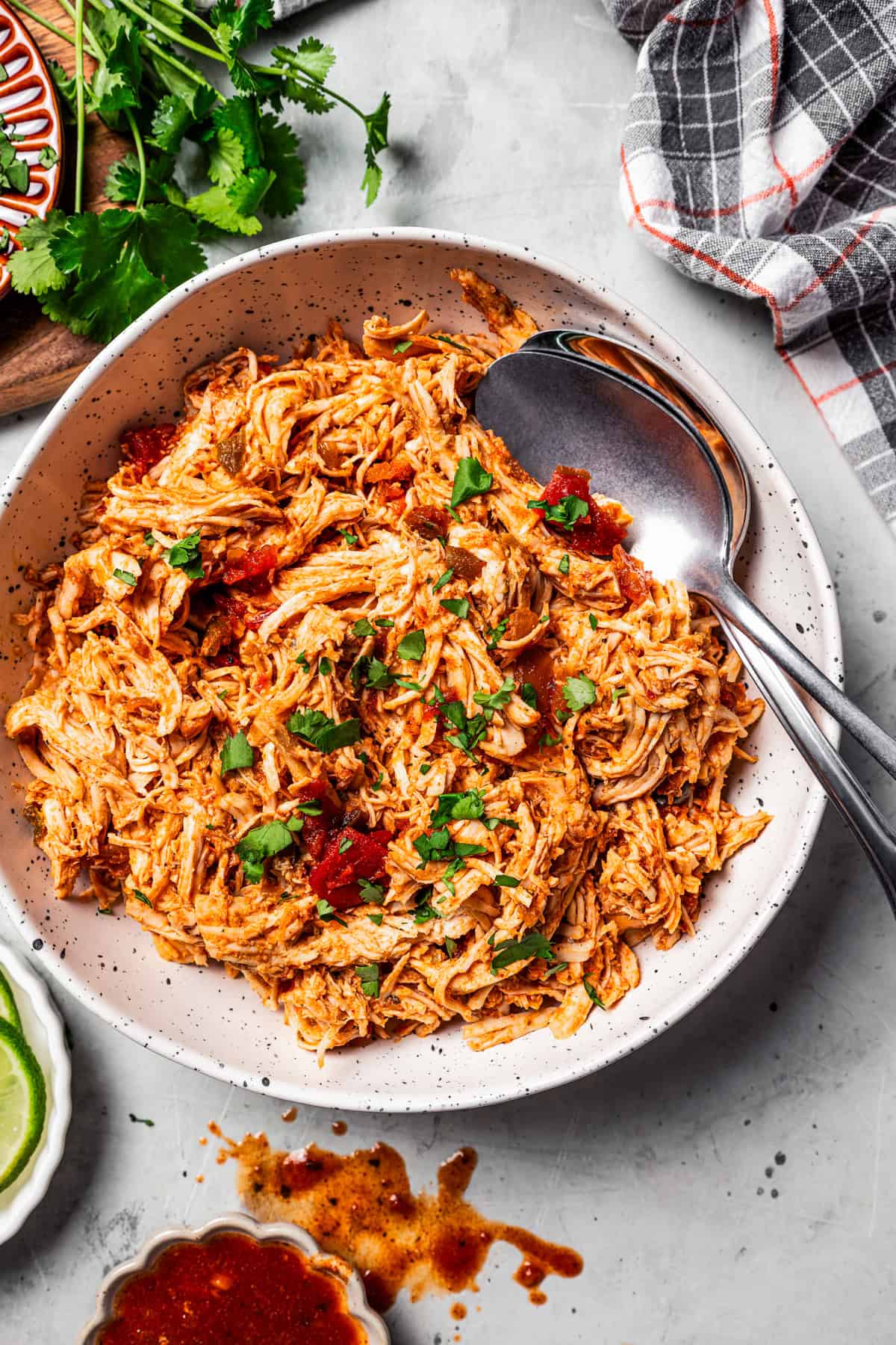 Overhead view of pulled chicken in a large bowl with two serving spoons.