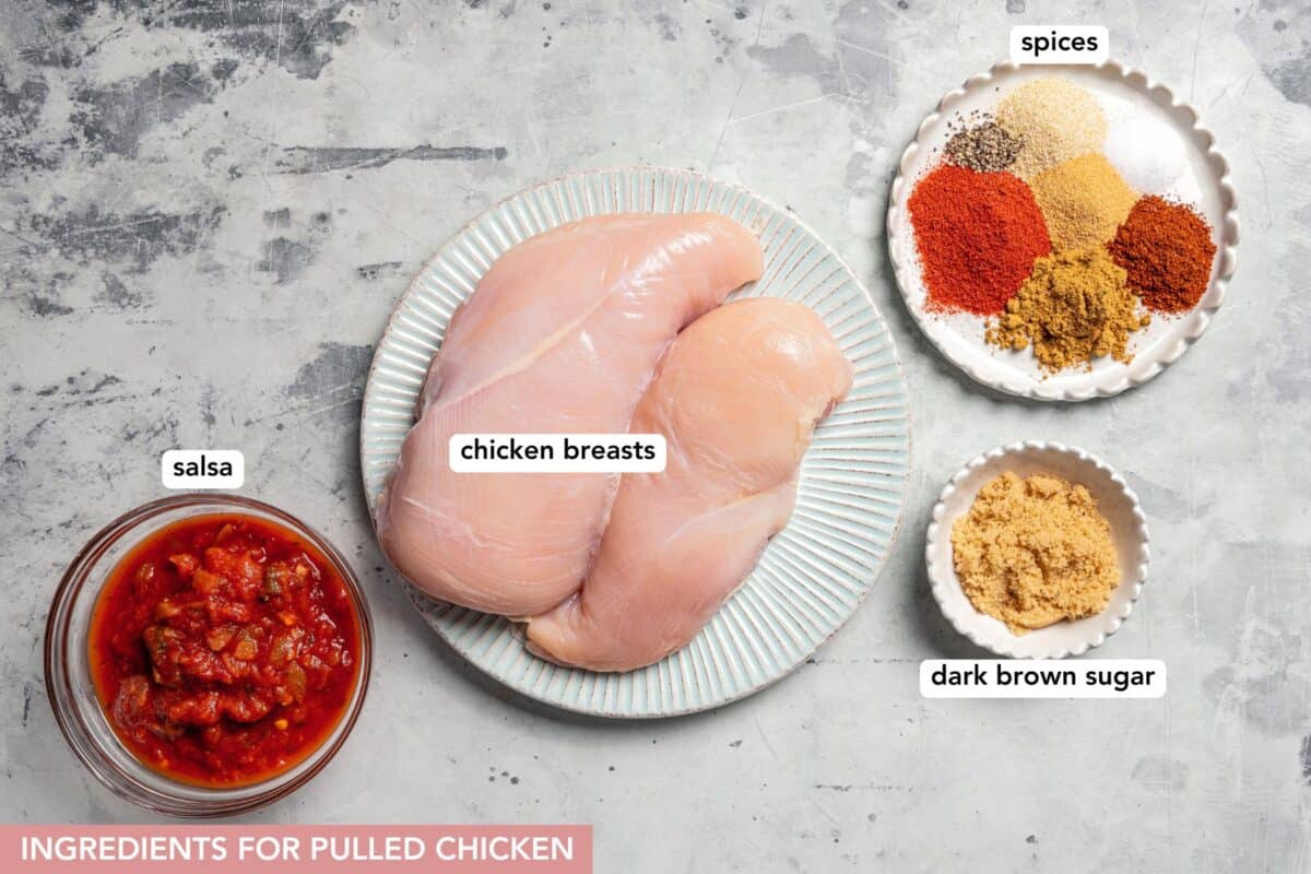 This slow cooker pulled chicken recipe is packed with zesty salsa and seasonings, delicious in tacos, pulled chicken sandwiches, and more! Pulled chicken ingredients with text labels overlaying each ingredient.