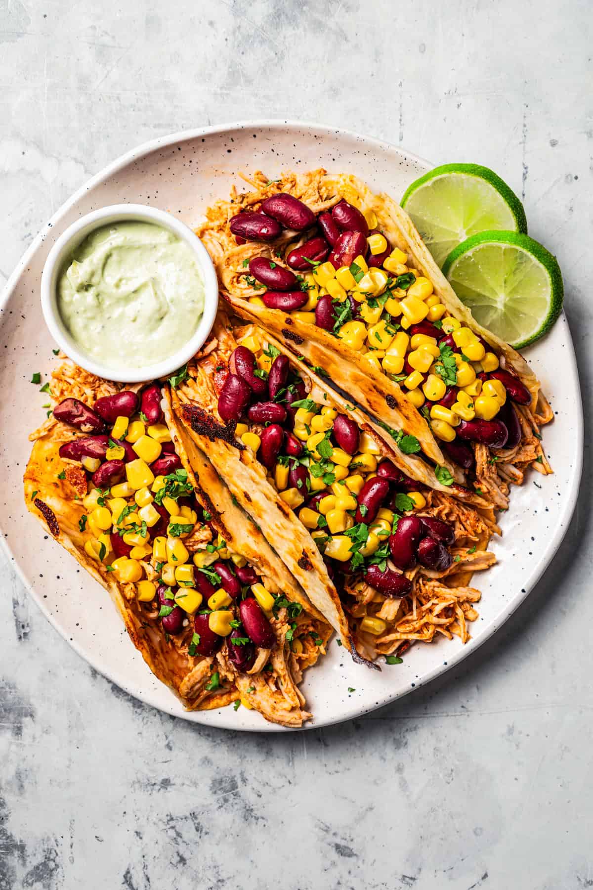 A plate of three pulled chicken tacos topped with corn and beans.