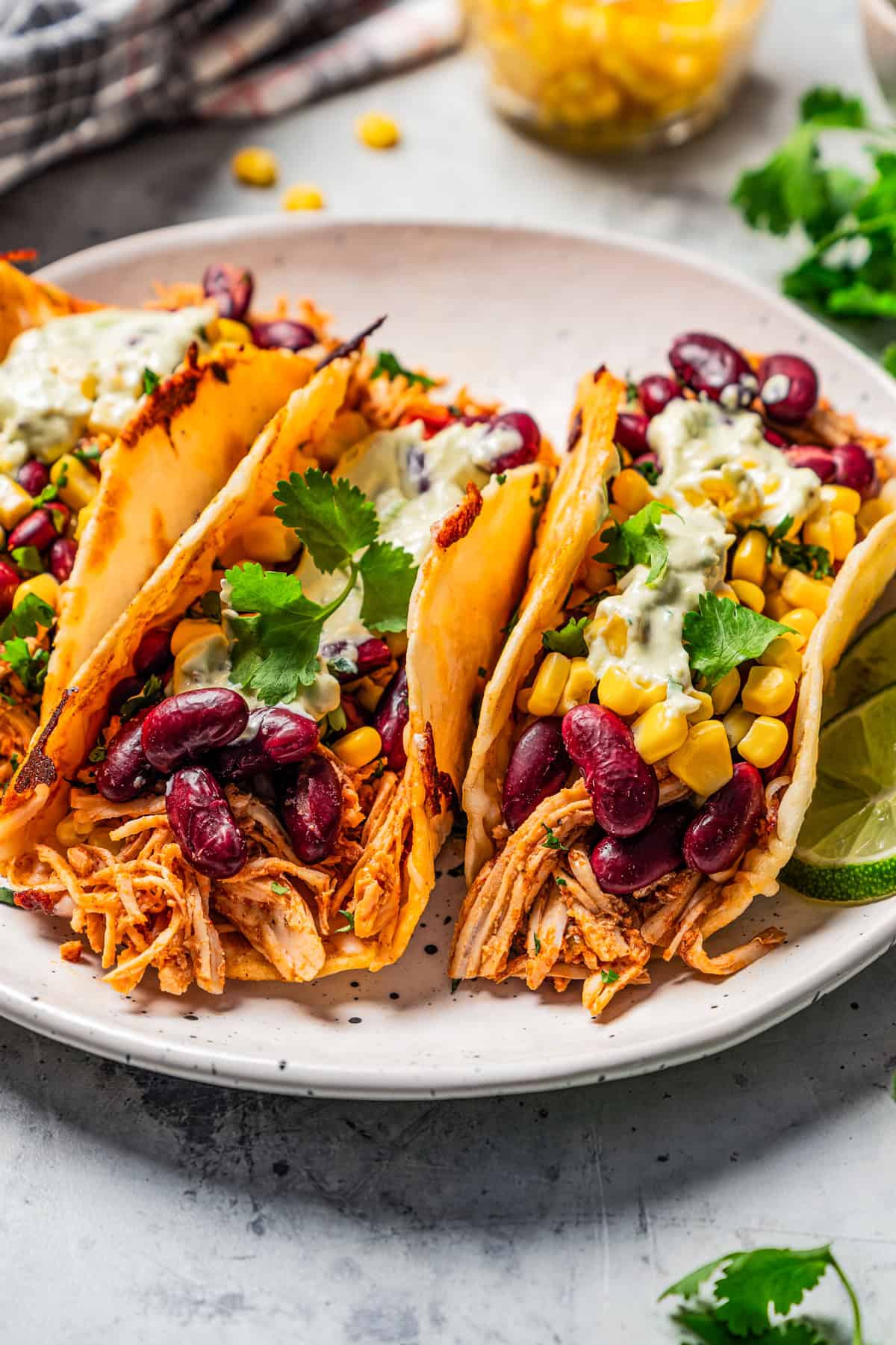 Three pulled chicken tacos topped with avocado sauce on a plate.