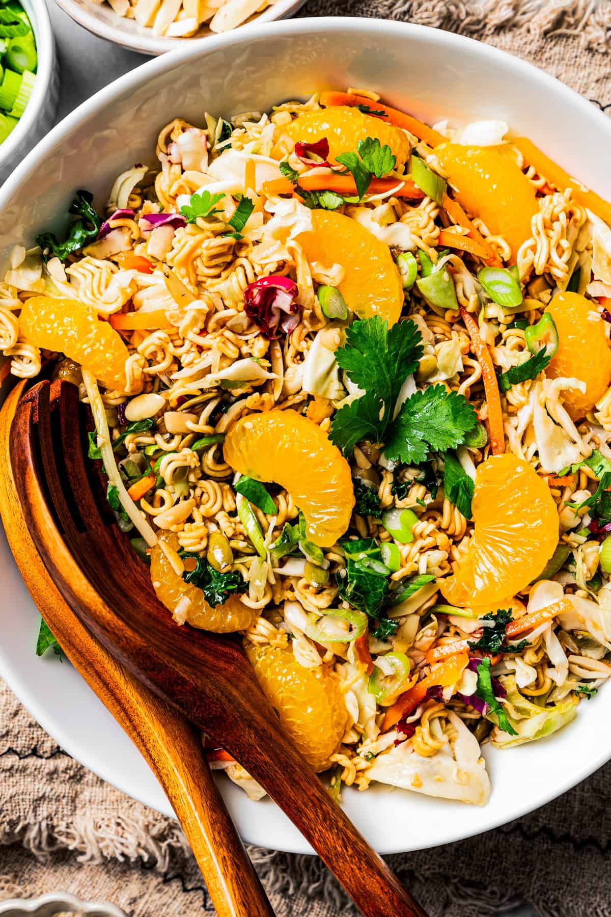 Ramen salad in a large bowl garnished with mandarin oranges, with two wooden salad tongs.