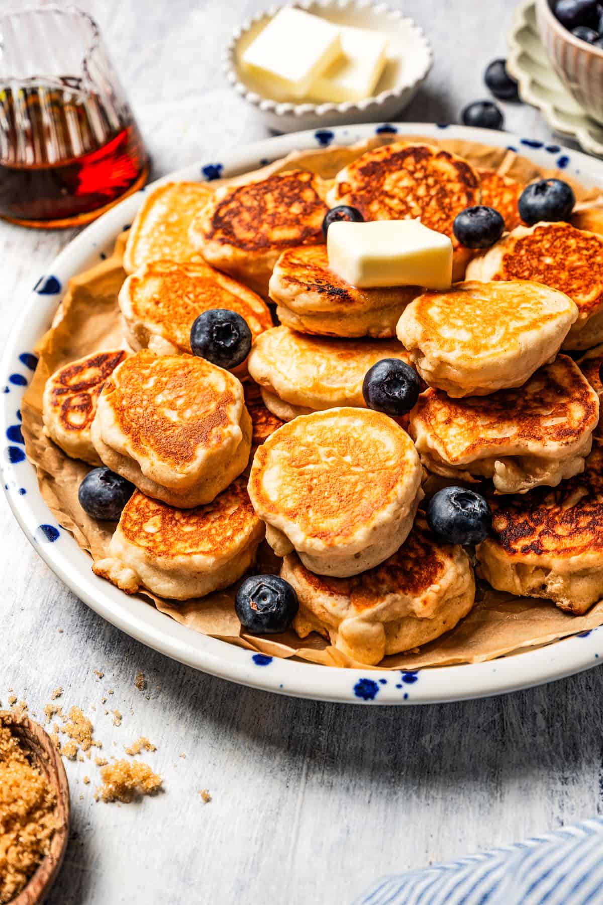 Small mini pancakes on a plate, topped with a pat of butter and blueberries.