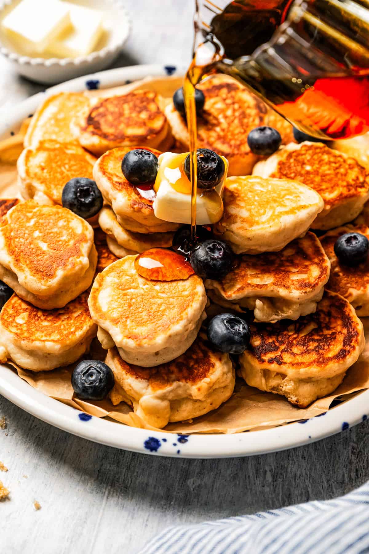 Pouring maple syrup over a plate of silver dollar pancakes.