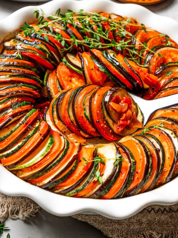 Ratatouille with slices of eggplant, zucchini, and tomatoes arranged accordion style in a round baking dish.