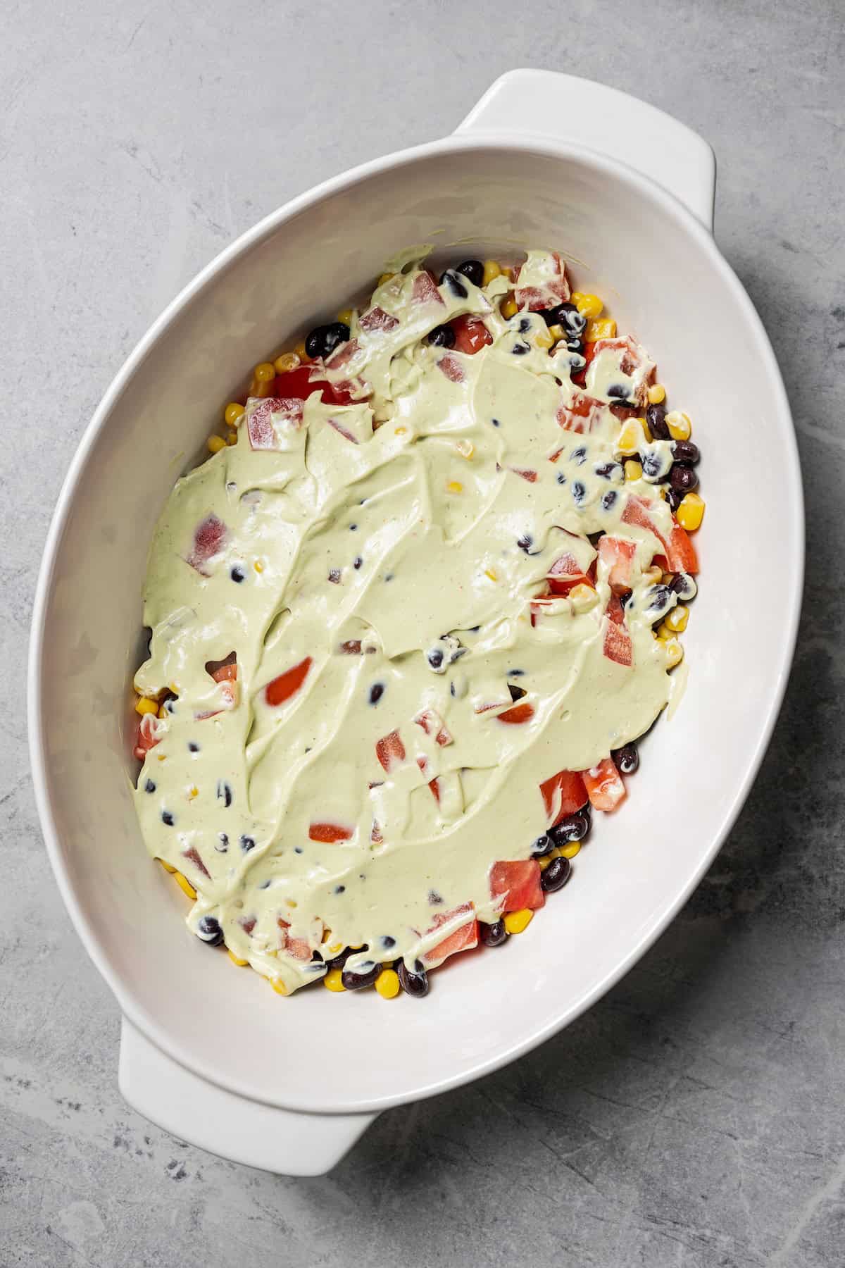 This Southwest avocado dip layers creamy avocado crema with a zesty mix of black beans, sweet corn, and tomatoes. Great with chips or veggies! Avocado crema spread over the beans-corn-tomato mixture in a serving dish.