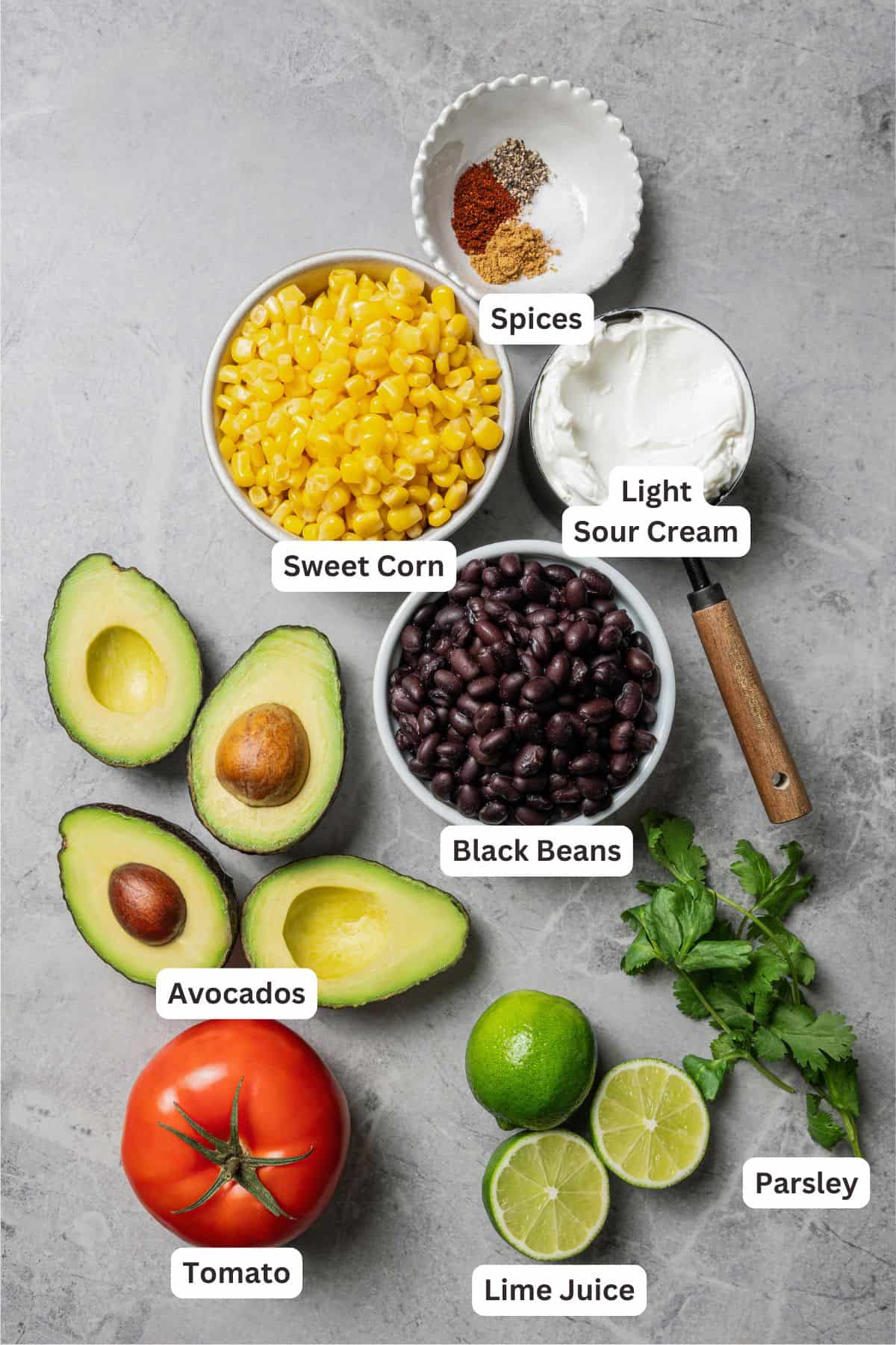 This Southwest avocado dip layers creamy avocado crema with a zesty mix of black beans, sweet corn, and tomatoes. Great with chips or veggies! Southwest avocado dip ingredients with text labels overlaying each ingredient.