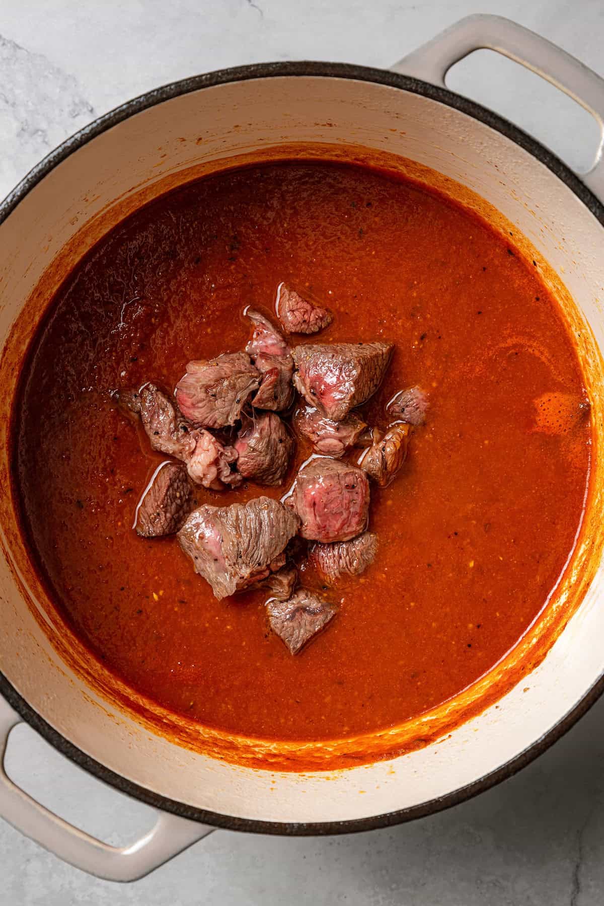 Overhead view of beef added back into a pot of madras curry sauce.