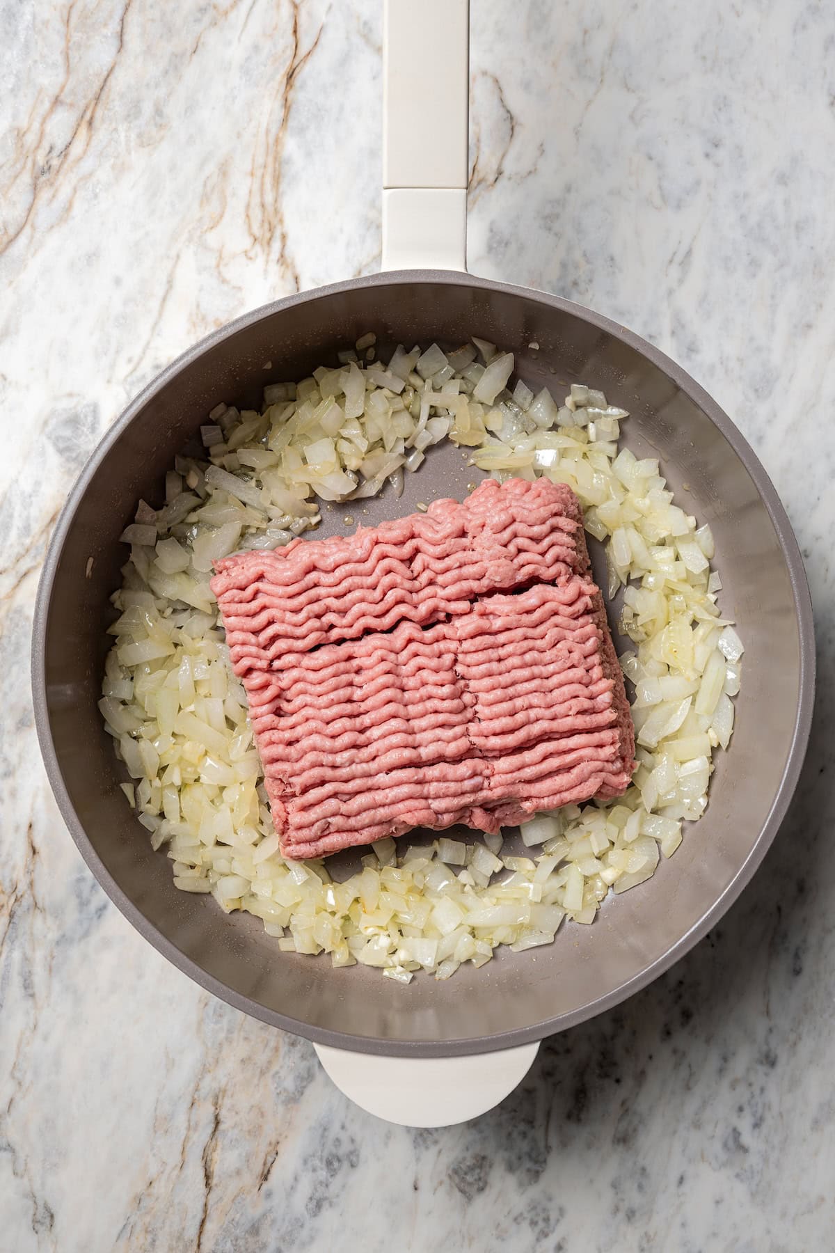 Ground turkey added to a skillet with sautéed onions.