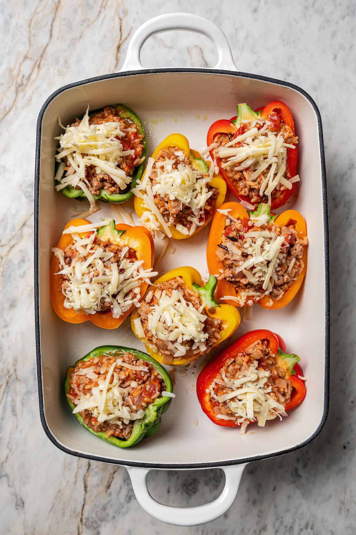 Esses pimentões recheados de peru moídos clássicos estão repletos de carne moída temperada, arroz selvagem e tomate suculento, coberto com queijo derretido e assado. Pimentão recheado de peru moído coberto com queijo ralado em uma assadeira.