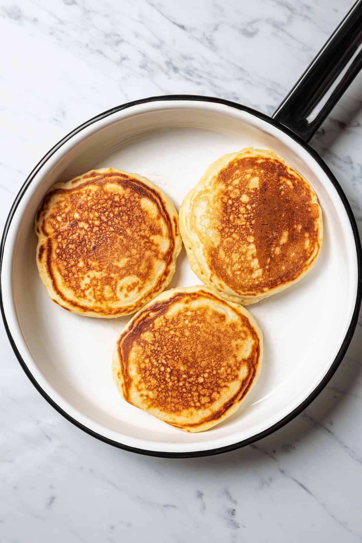Three lemon ricotta pancakes cooking in a skillet.