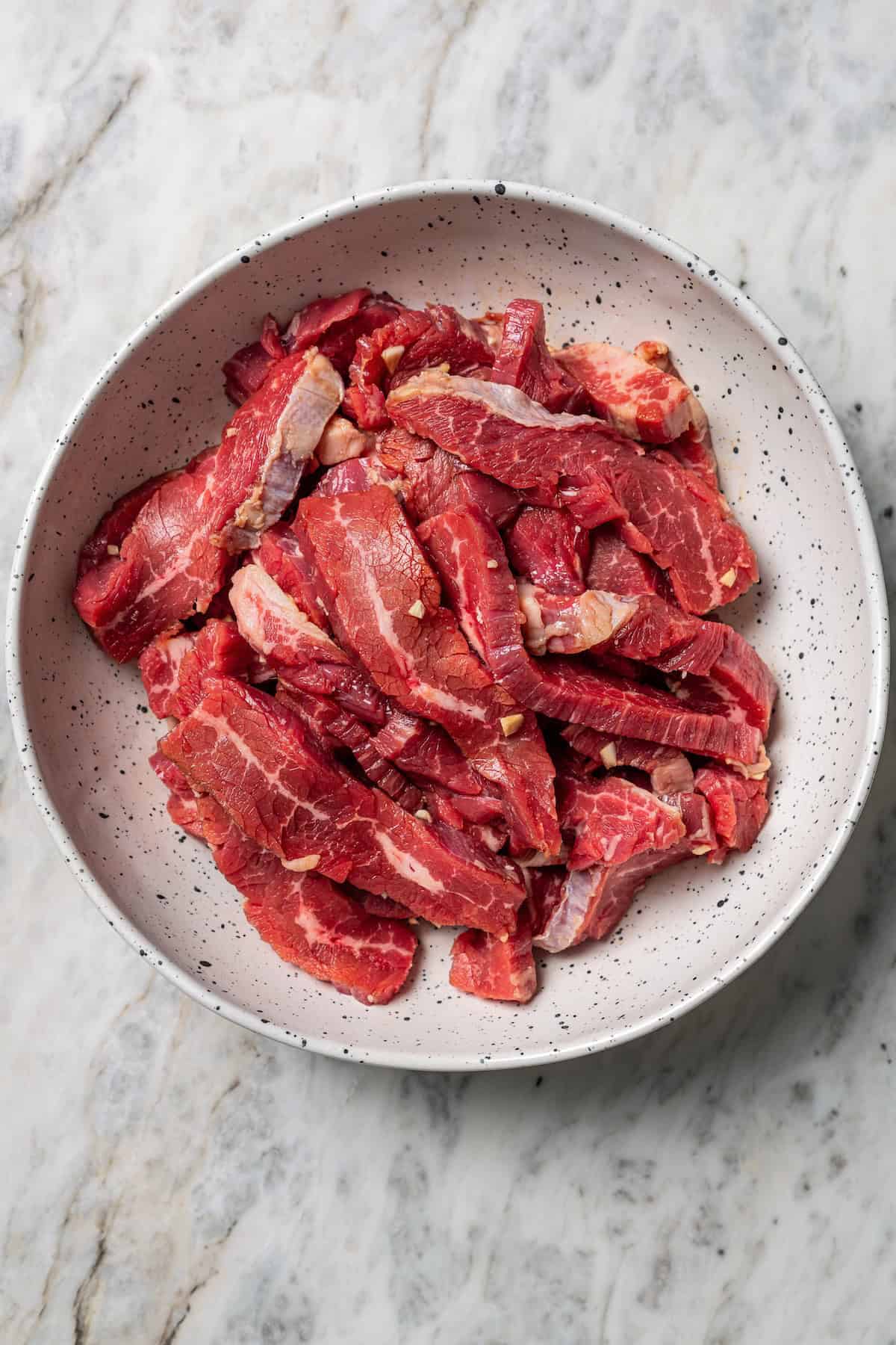 Lomo saltado is a Peruvian stir-fry with juicy marinated beef strips, onions, tomatoes, and fiery chilies, served with crispy French fries. Marinated steak strips in a bowl.