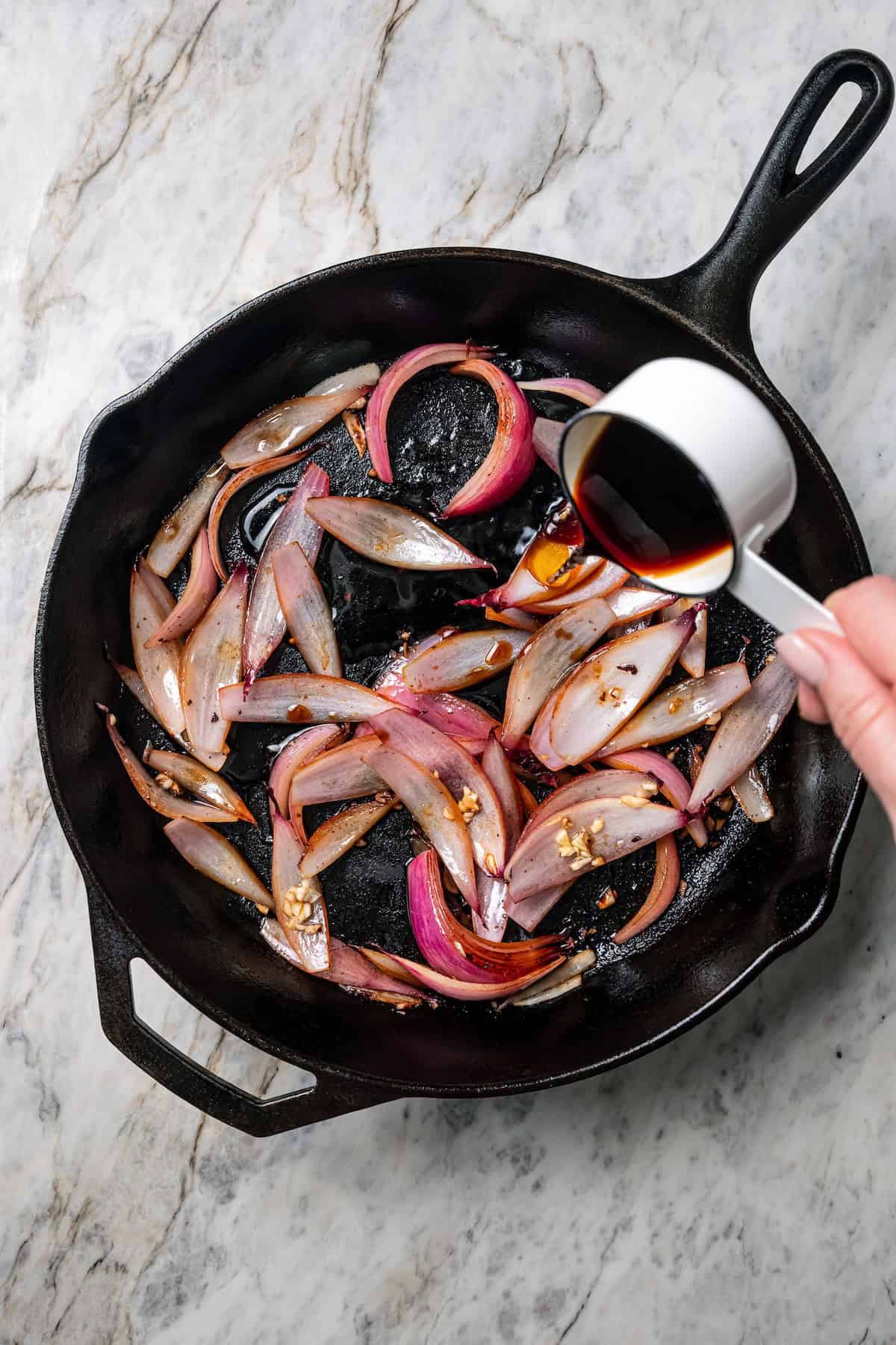 Lomo saltado is a Peruvian stir-fry with juicy marinated beef strips, onions, tomatoes, and fiery chilies, served with crispy French fries. Soy sauce added to sautéed red onions in a cast iron skillet.