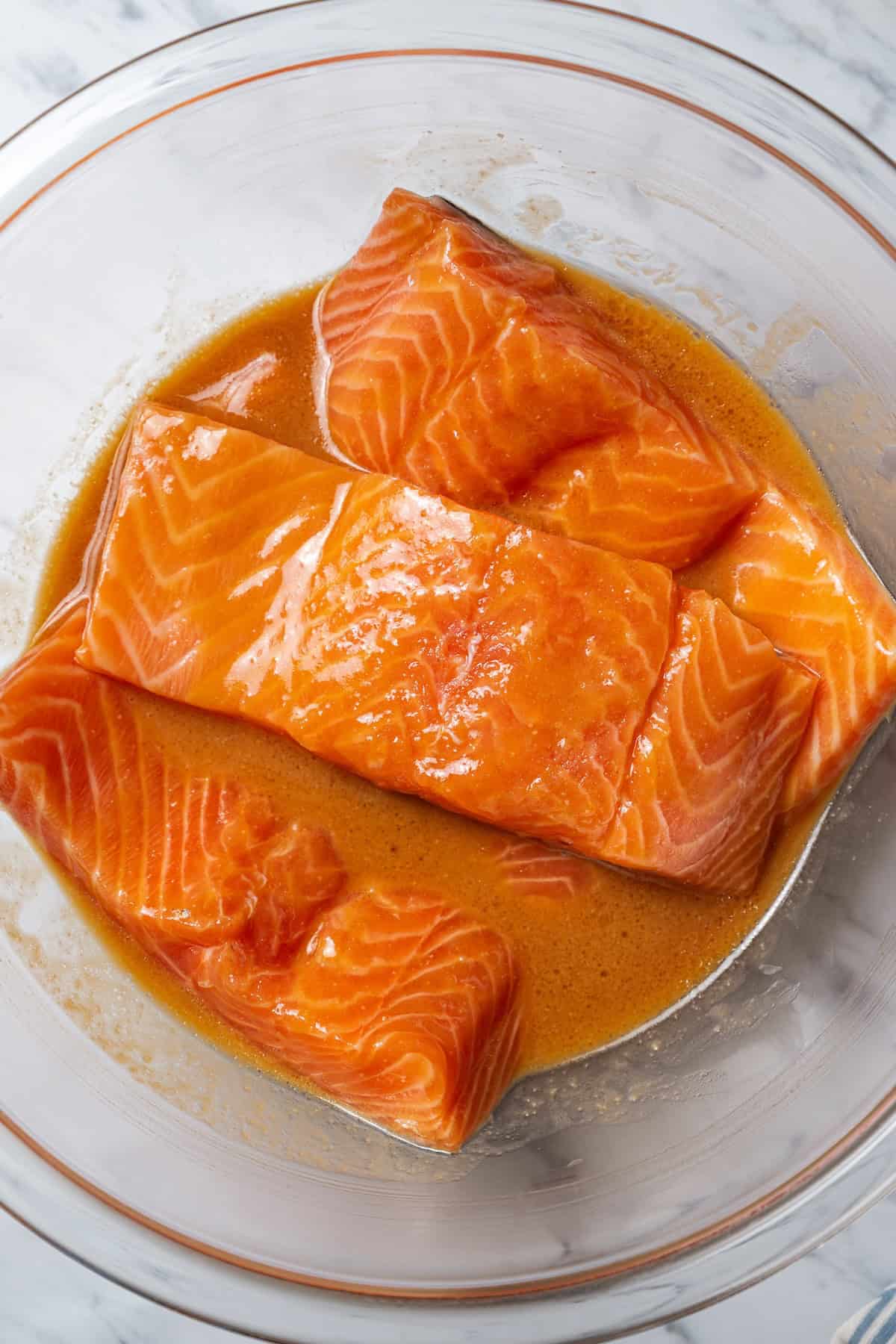 This sweet and savory miso salmon is caramelized outside and tender and flaky inside. Serve it with rice for a quick, easy salmon dinner! Salmon fillets marinating in a bowl with miso glaze.