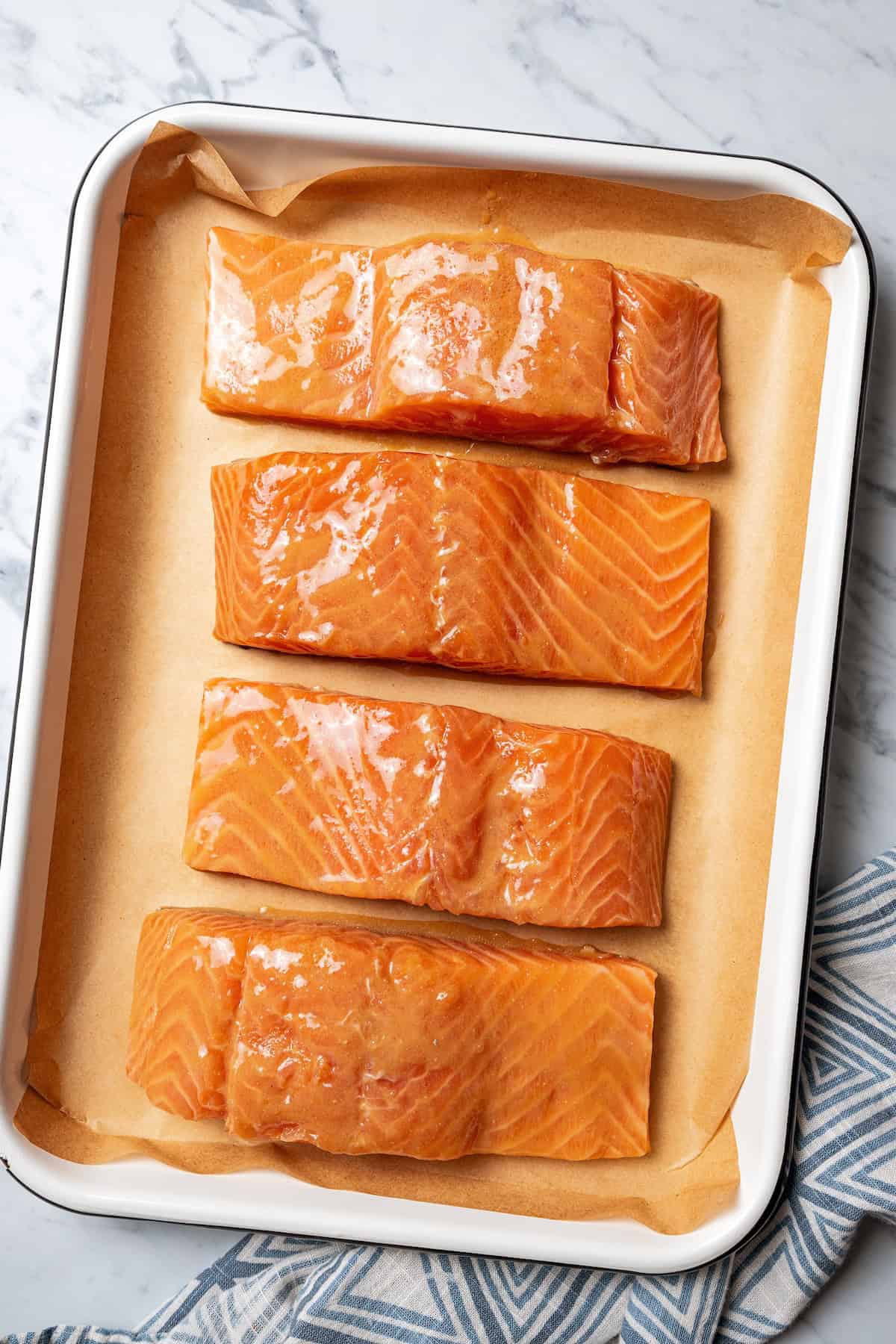 This sweet and savory miso salmon is caramelized outside and tender and flaky inside. Serve it with rice for a quick, easy salmon dinner! Marinated salmon fillets on a lined baking sheet.