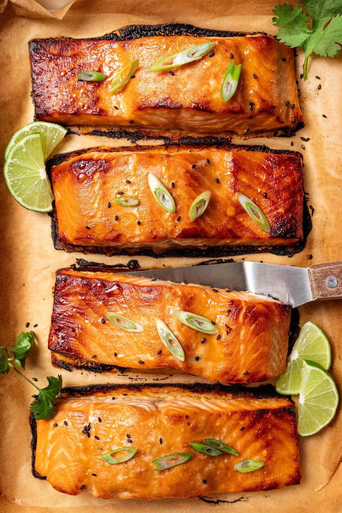 This sweet and savory miso salmon is caramelized outside and tender and flaky inside. Serve it with rice for a quick, easy salmon dinner! Overhead view of miso salmon garnished with sesame seeds and scallions on a lined baking tray, with a spatula tucked under one of the fillets.