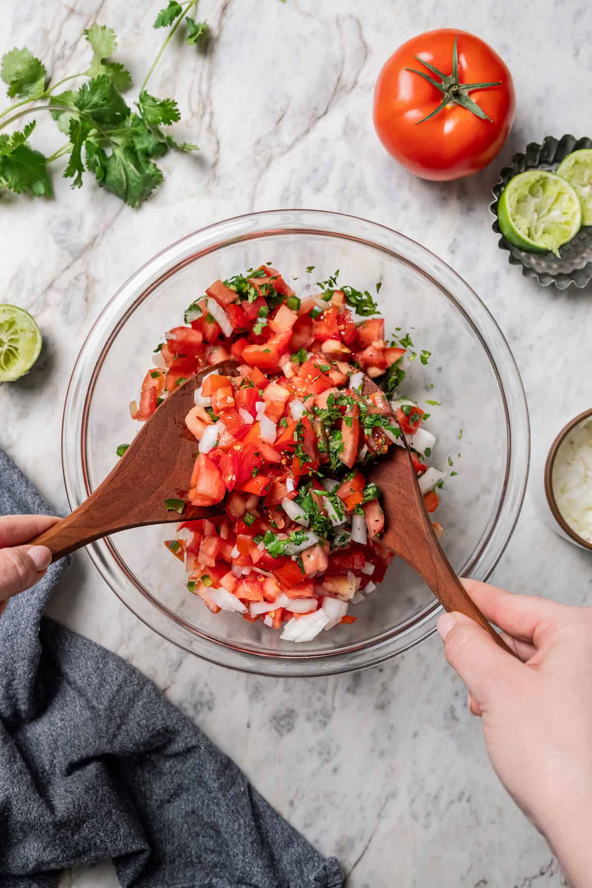 Pico de gallo ingredients being tossed together in a bowl with two wooden spoons.